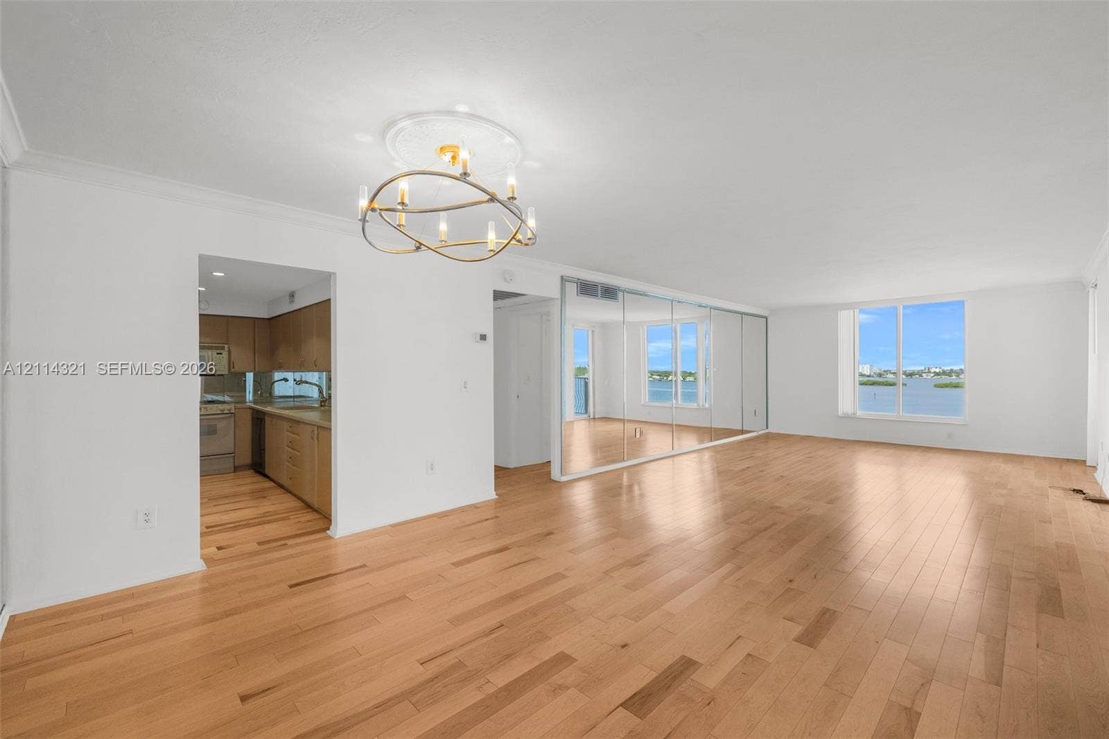 10350 W Bay Harbor Drive, #9C, Bay Harbor Islands, FL 33154 Open-concept living space featuring wood-finish flooring, a modern multi-bulb chandelier, mirrored wall paneling, and large windows with water scenery