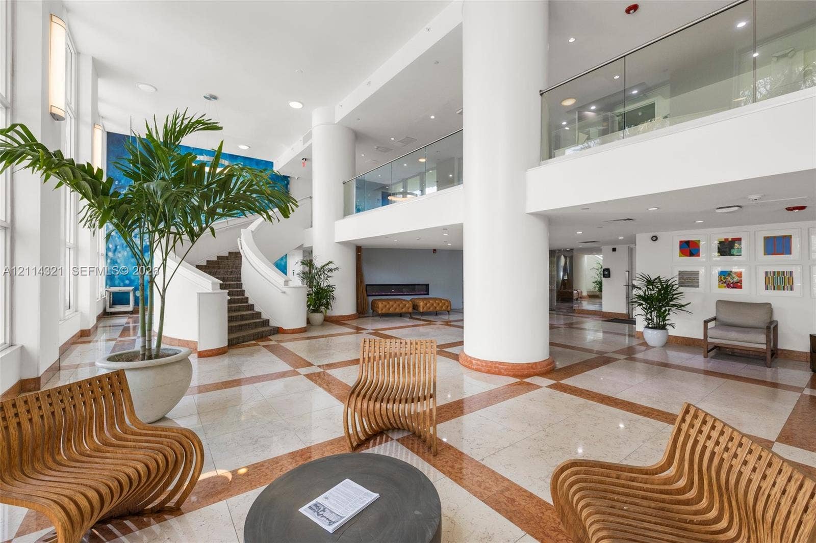 10350 W Bay Harbor Drive, #9C, Bay Harbor Islands, FL 33154 Grand lobby featuring a double-height ceiling, polished tile flooring with inlaid stone detailing, a sweeping staircase with a curved railing, and a glass-paneled mezzanine