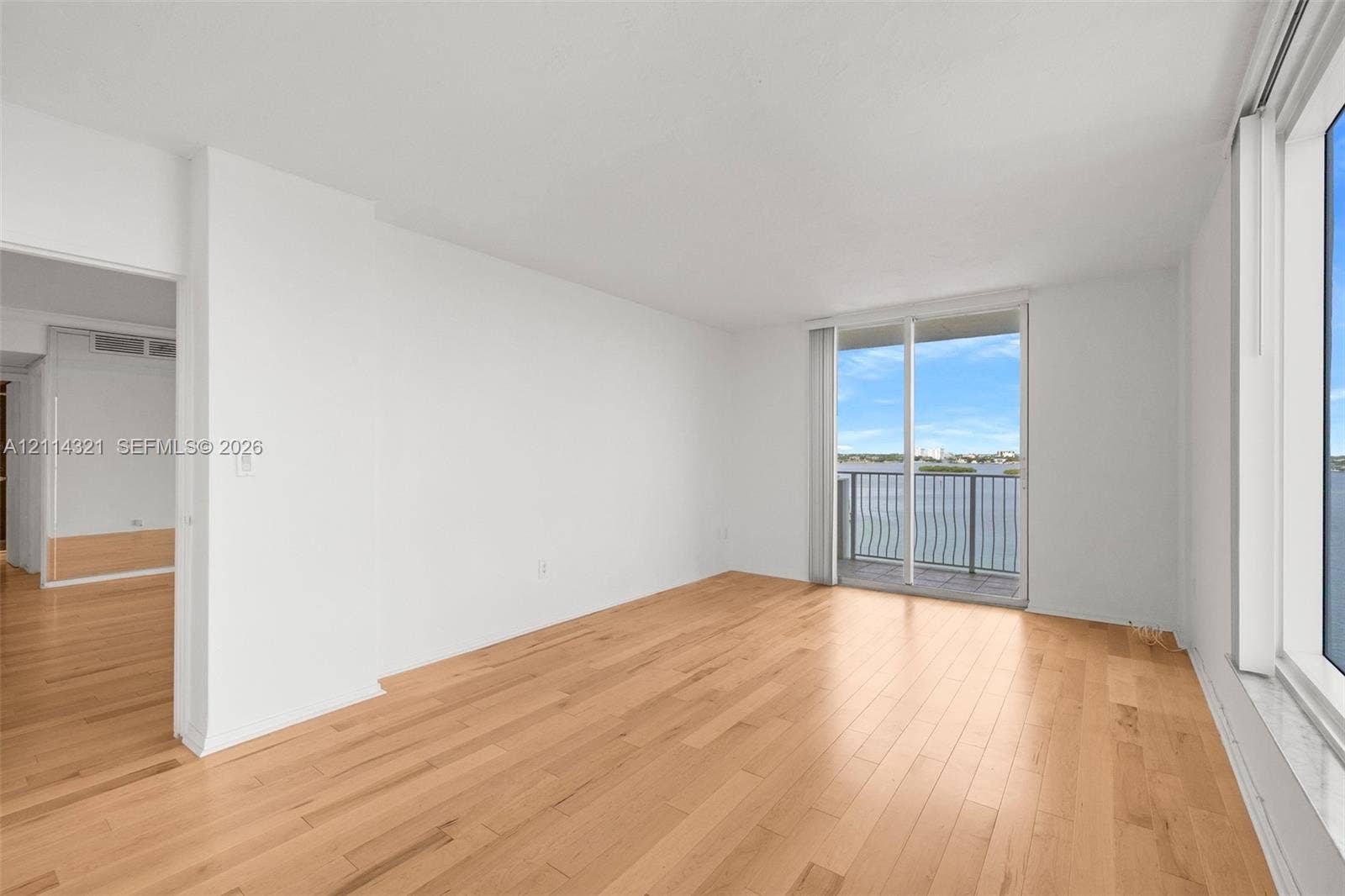 10350 W Bay Harbor Drive, #9C, Bay Harbor Islands, FL 33154 Living area featuring light-toned wood-finish flooring, floor-to-ceiling windows, and a glass sliding door opening to a private balcony with water scenery