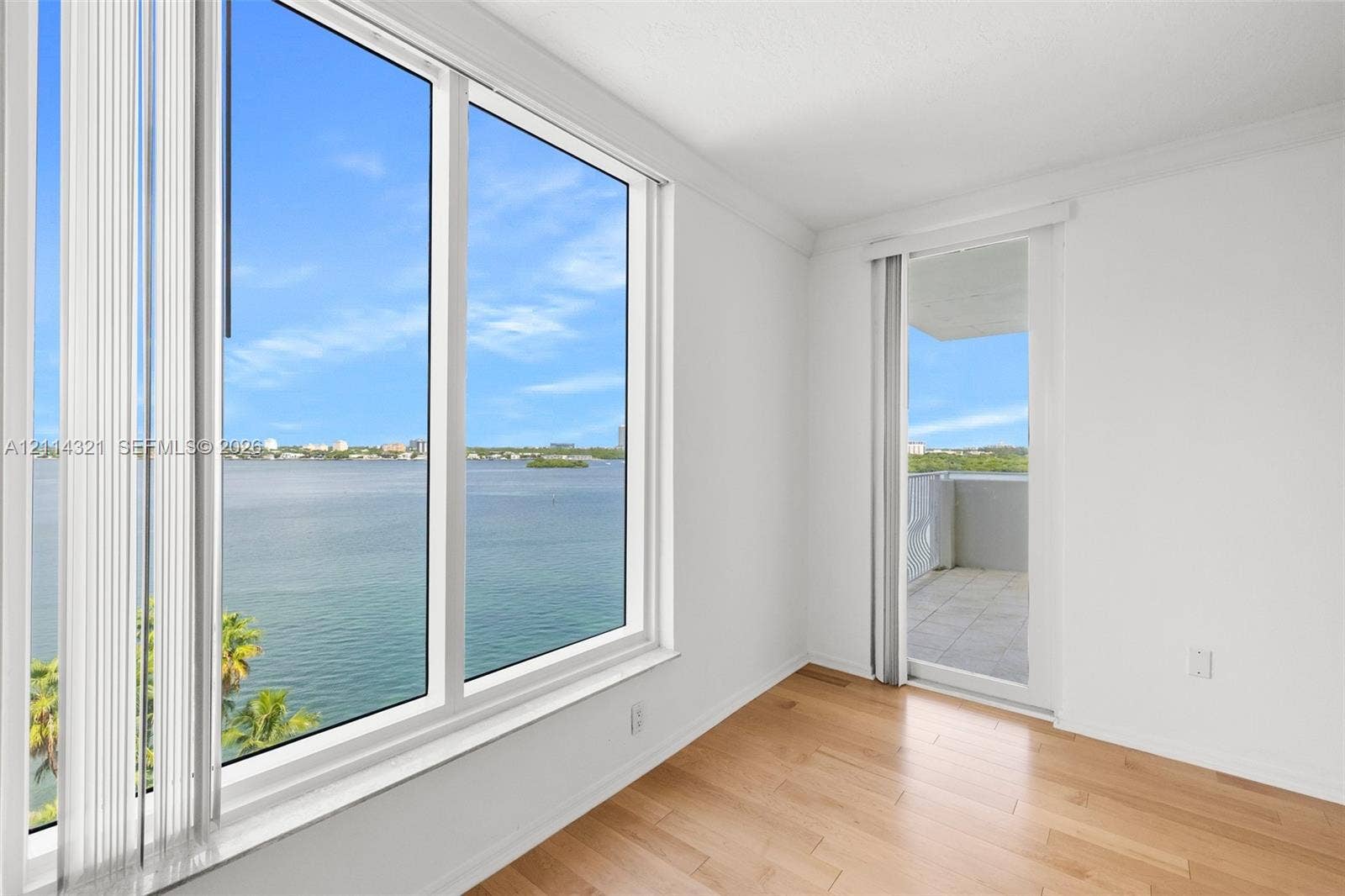 10350 W Bay Harbor Drive, #9C, Bay Harbor Islands, FL 33154 Large, wall-to-ceiling windows, wood-finish flooring, and a sliding glass door leading to a private balcony overlooking the water