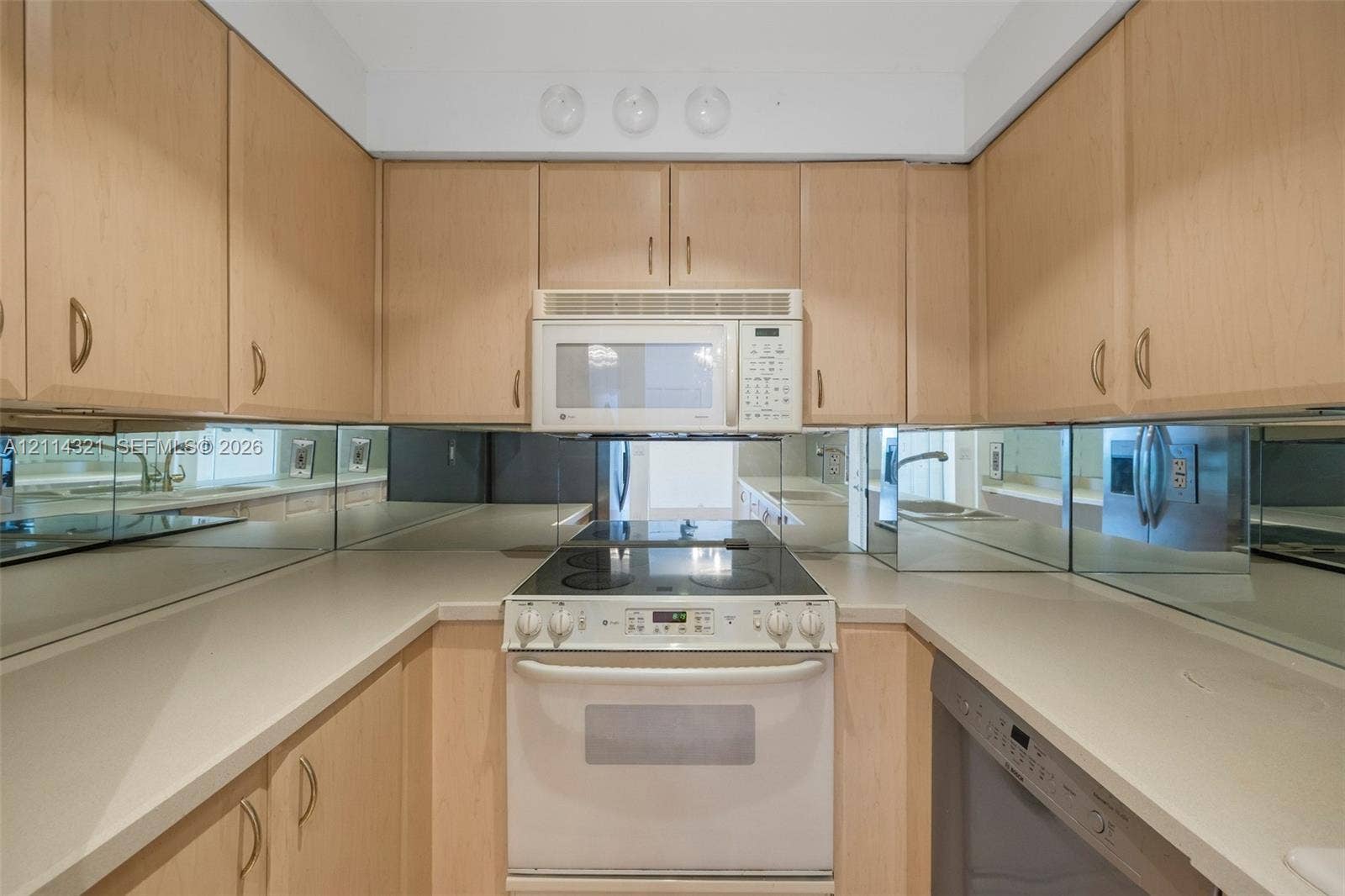 10350 W Bay Harbor Drive, #9C, Bay Harbor Islands, FL 33154 Kitchen featuring light wood-finish cabinetry, solid surface countertops, a mirrored backsplash, and a built-in over-the-range microwave