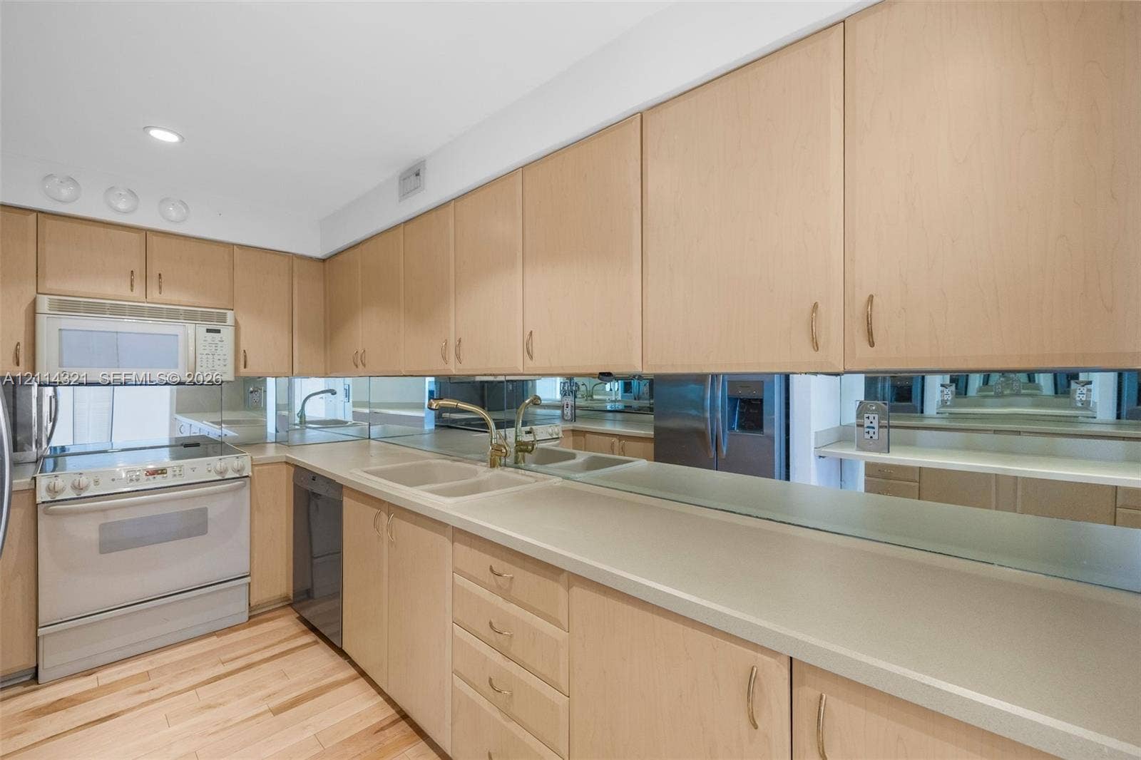 10350 W Bay Harbor Drive, #9C, Bay Harbor Islands, FL 33154 Kitchen featuring light-finish cabinetry, neutral solid-surface countertops, wood-finish flooring, a mirrored backsplash, and an integrated microwave