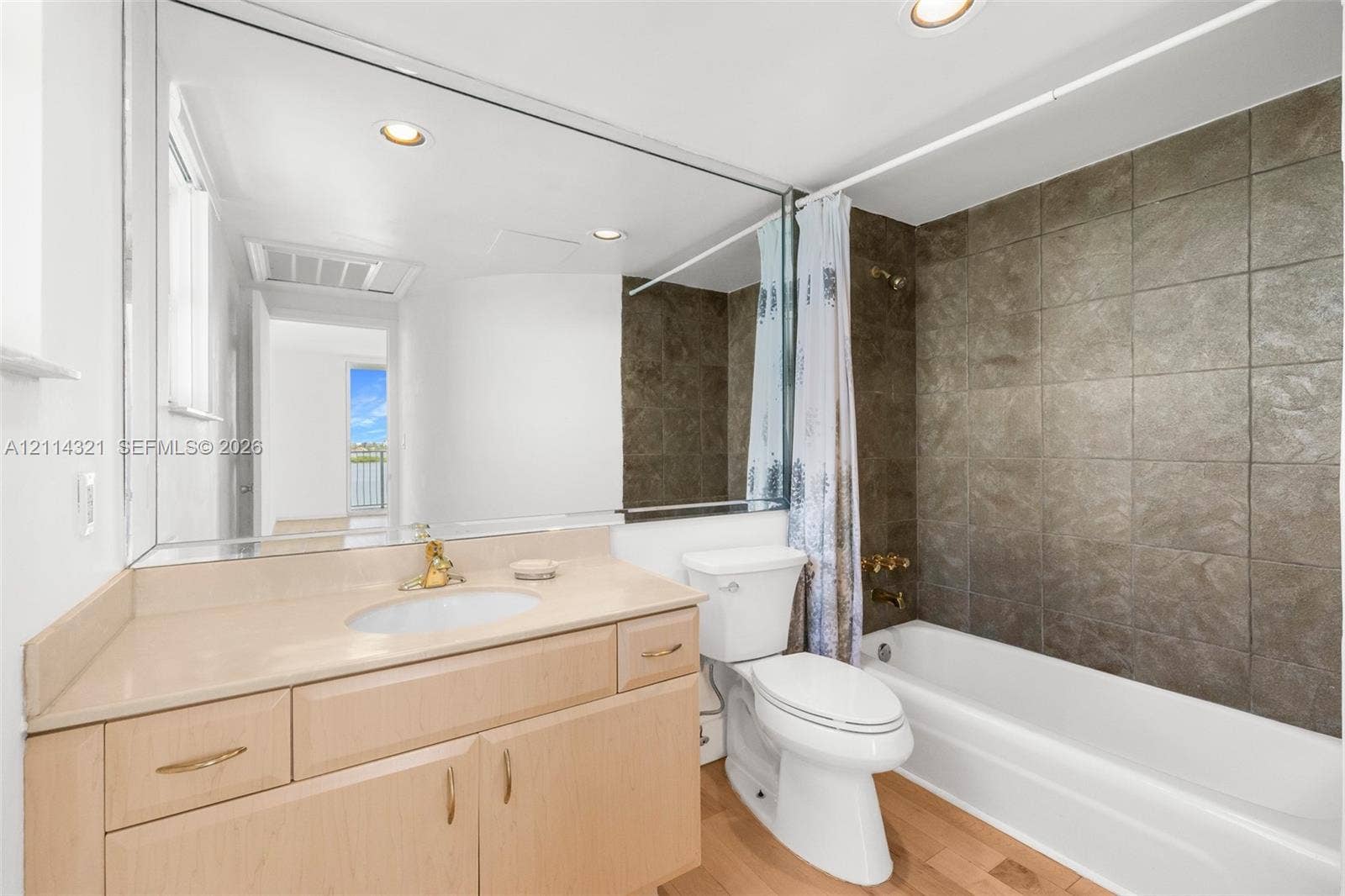 10350 W Bay Harbor Drive, #9C, Bay Harbor Islands, FL 33154 Bathroom featuring a vanity with an integrated countertop and sink, large wall-spanning mirror, wood-finish flooring, and a bathtub with tile surround