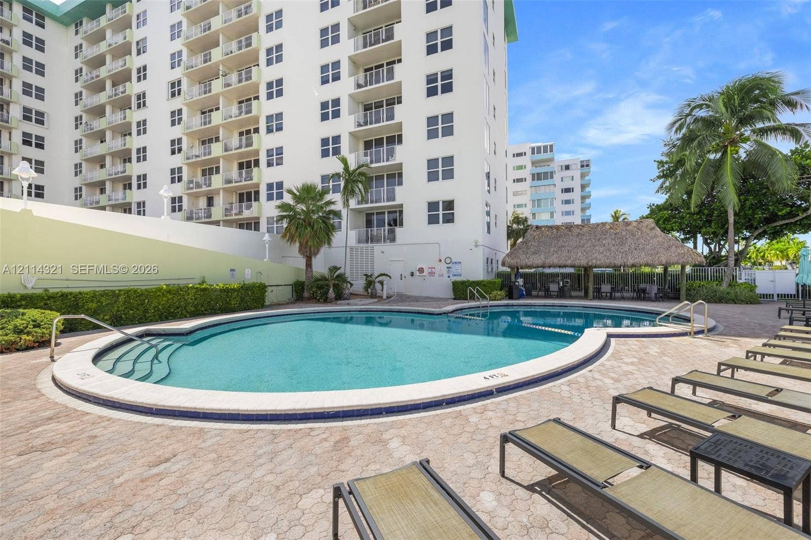 10350 W Bay Harbor Drive, #9C, Bay Harbor Islands, FL 33154 Curved outdoor swimming pool with built-in steps, paver pool deck, and thatched-roof tiki hut