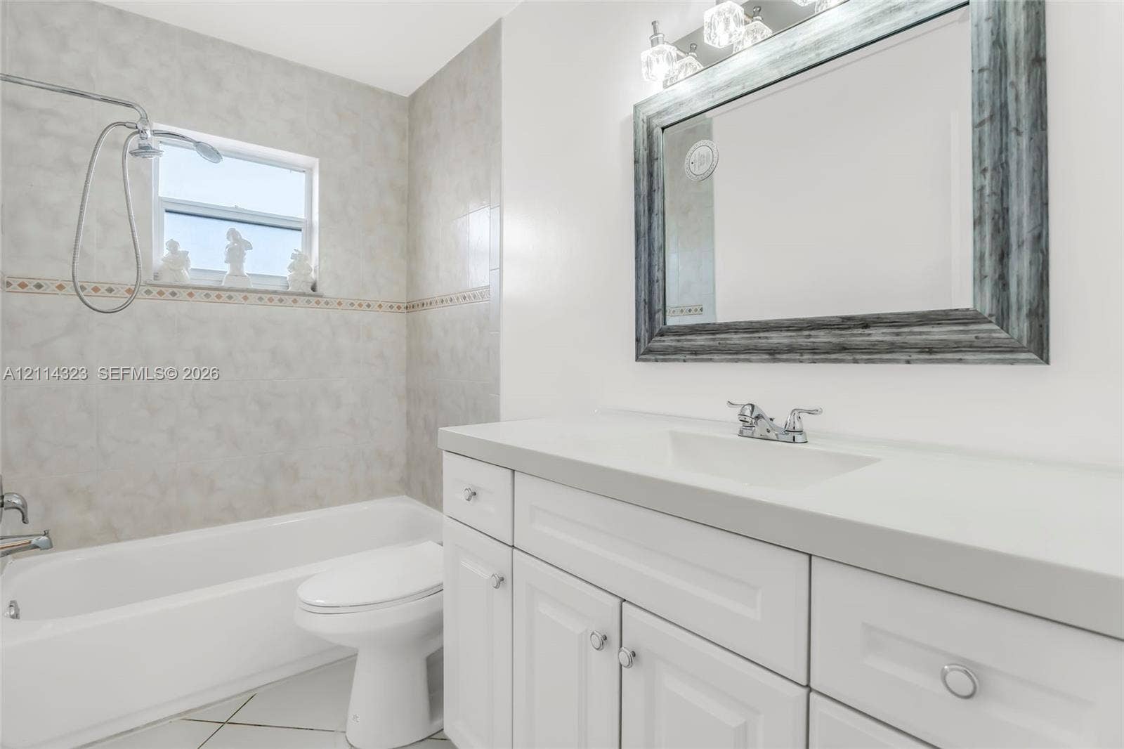Bathroom featuring white cabinetry, solid-surface countertop, integrated vanity sink, wall-mounted mirror, and tile-surround tub