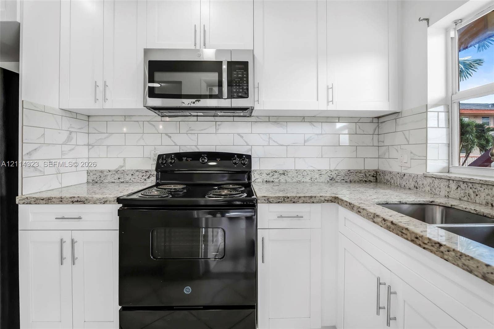 Kitchen featuring white Shaker-style cabinetry, stone-finish countertops, stainless steel microwave, black range, and stone-patterned subway tile backsplash