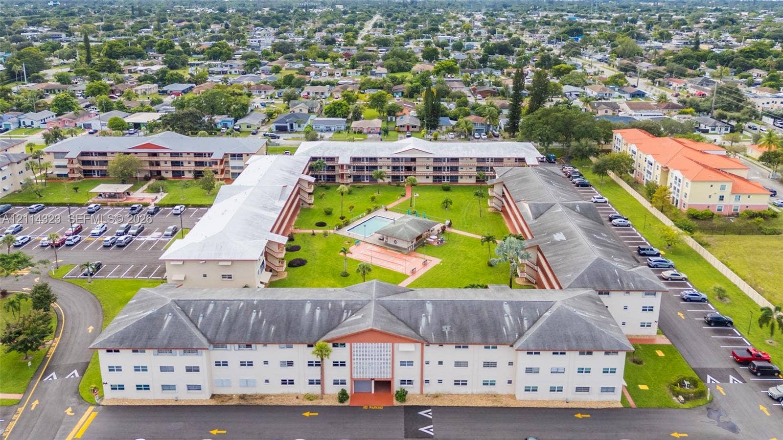 Aerial perspective of a multi-building residential complex featuring a central courtyard, a swimming pool, a covered pavilion, and dedicated surface parking