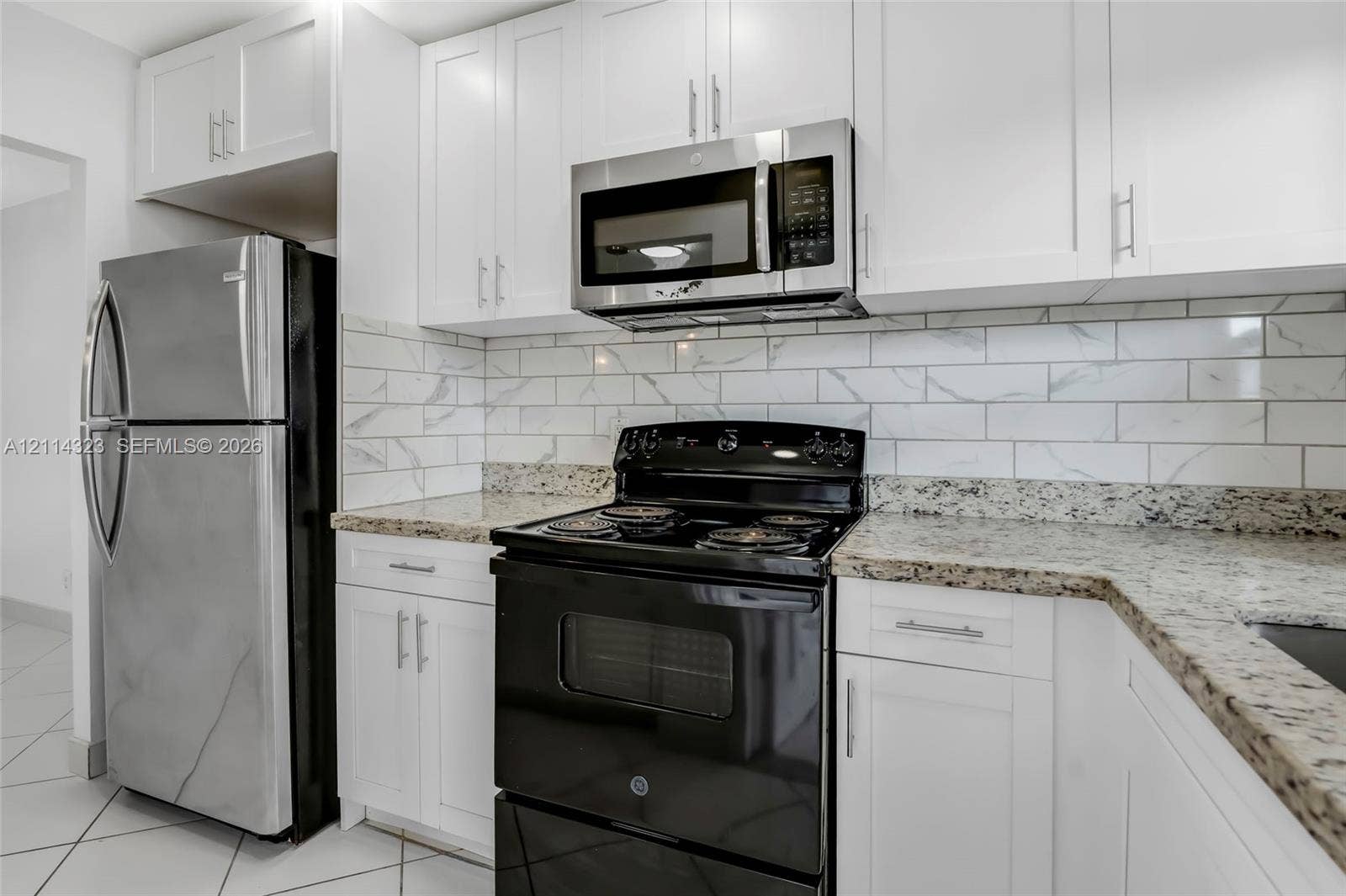 Kitchen featuring white shaker-style cabinetry, stone-finish countertops, subway tile backsplash, stainless steel microwave, and stone-tile flooring