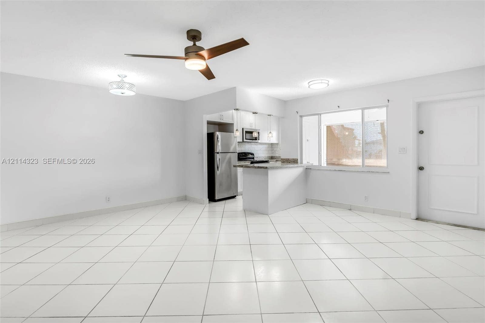 Open-concept interior featuring light-toned tiled flooring, a kitchen peninsula with stone-finish countertops, stainless steel appliances, a modern ceiling fan, and recessed lighting fixtures