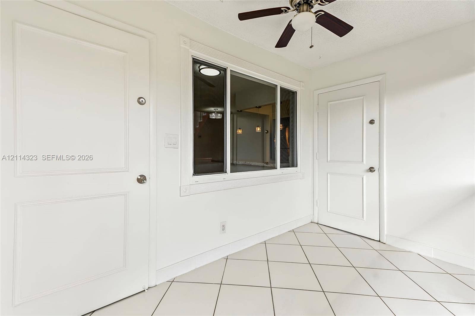 Diagonal tile flooring, two solid-panel doors, a central multi-pane window, and a ceiling-mounted light fixture with a fan