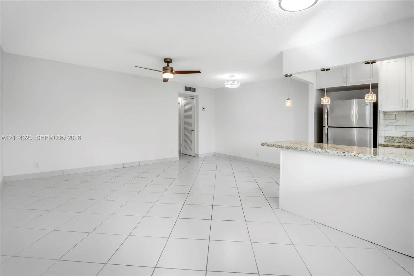 Open-concept interior featuring large-format tile flooring, a stone-surfaced breakfast bar, pendant lighting, and a ceiling fan