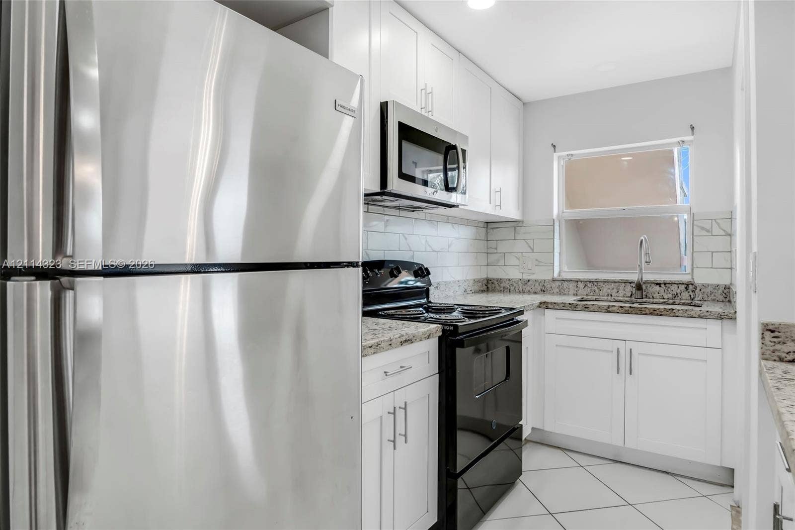 Kitchen featuring white shaker-style cabinetry, stone-finish countertops, subway tile backsplash, stainless steel refrigerator, and built-in microwave