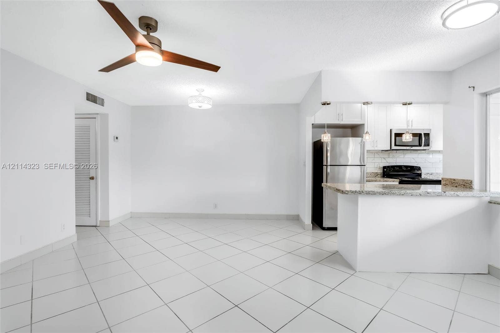Kitchen featuring white cabinetry, stone countertops, a subway tile backsplash, and stainless steel appliances, complemented by large-format tile flooring and overhead designer lighting