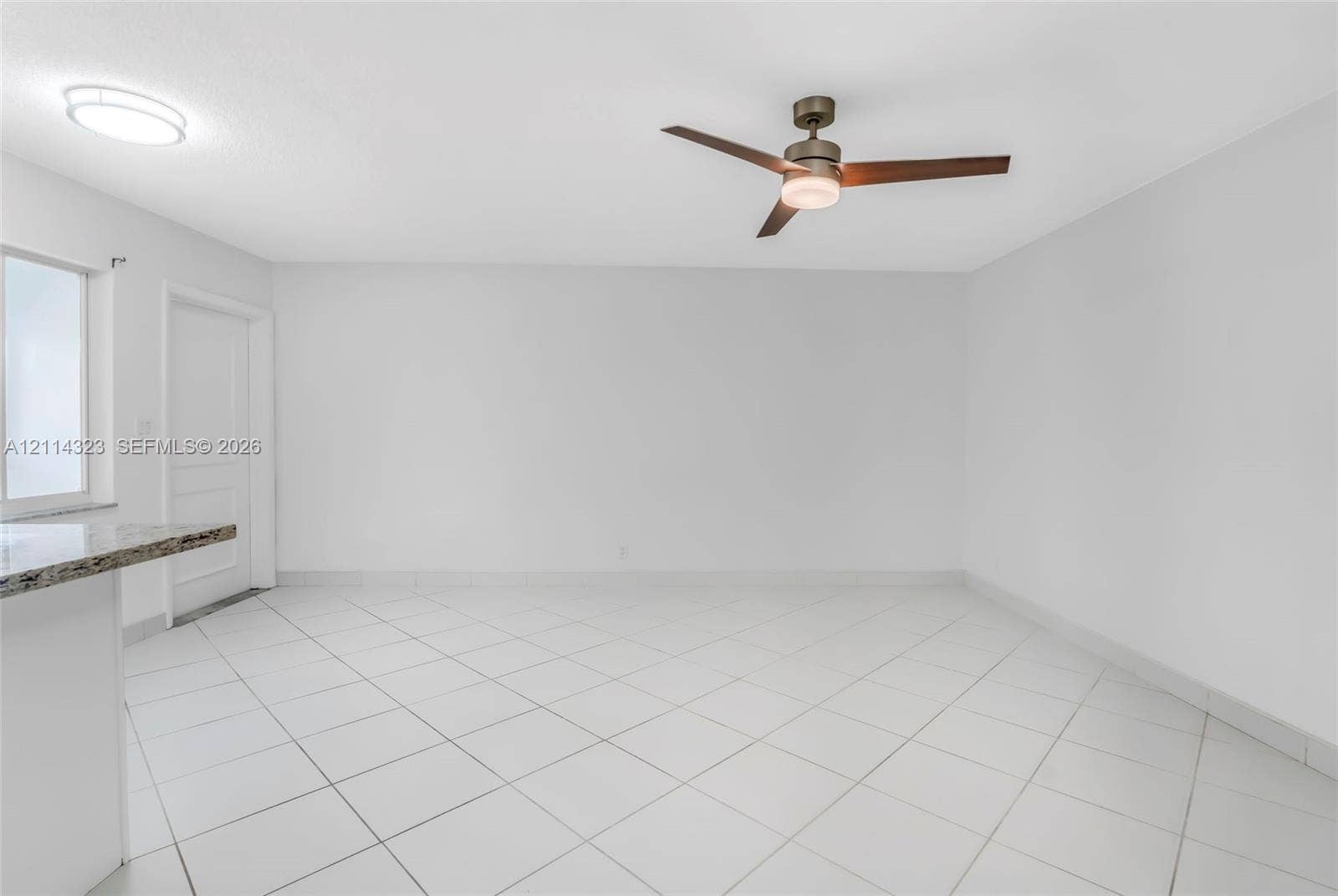 Neutral interior featuring large-format diagonal tile flooring, a modern three-blade ceiling fan with integrated lighting, a flush-mount circular ceiling fixture, and a granite-topped peninsula