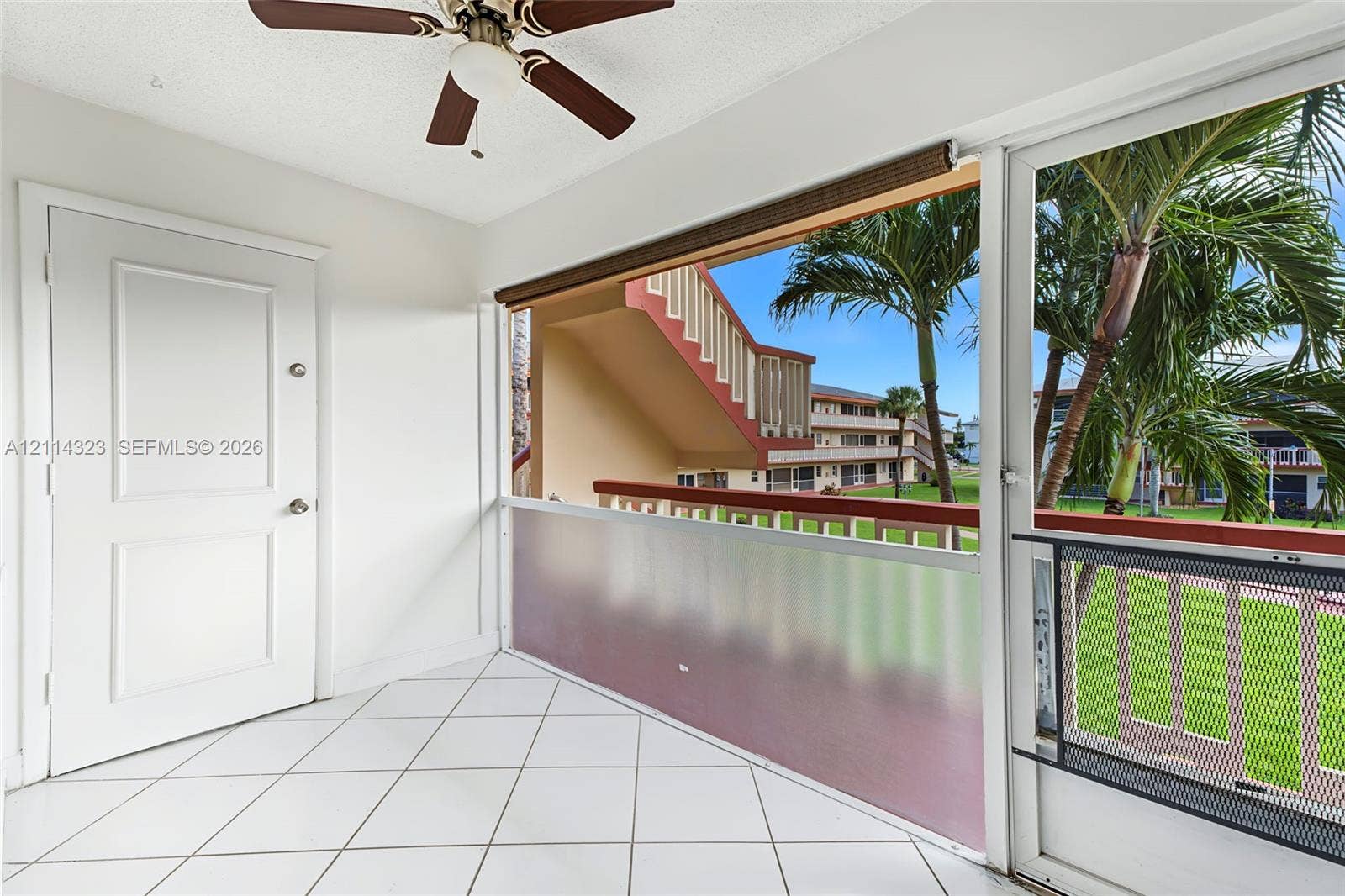 Enclosed balcony featuring white tile flooring, ceiling fan, and privacy screening