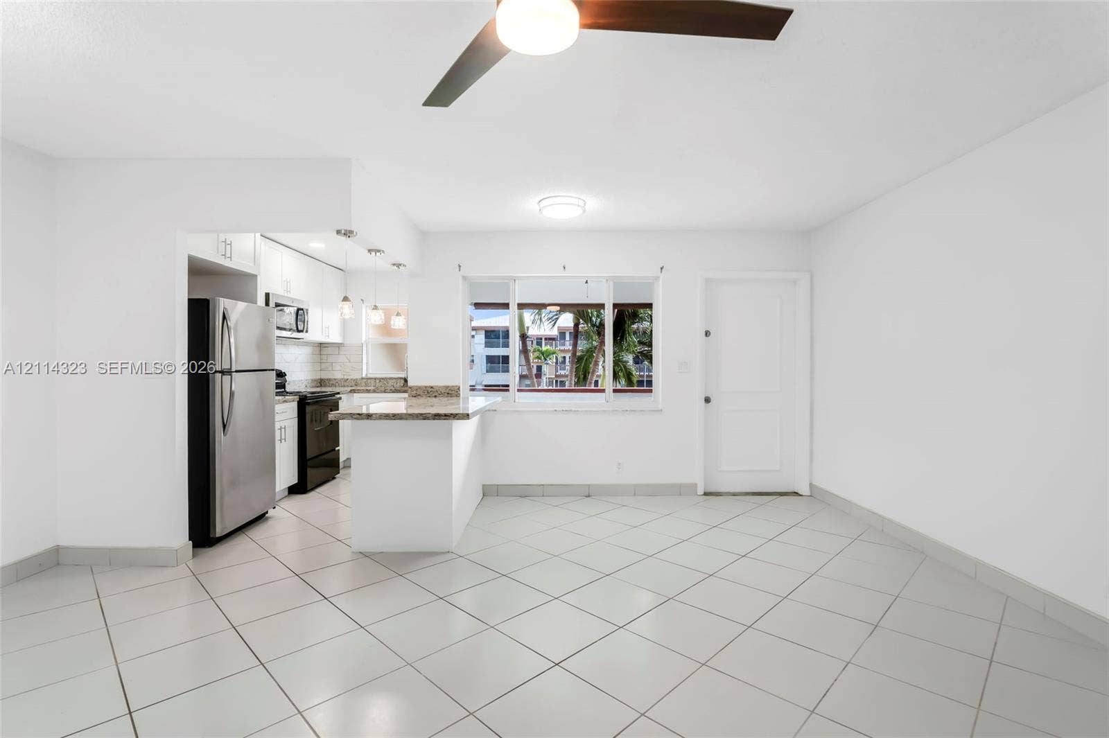 Kitchen featuring stone-finish countertops, stainless steel refrigerator, white cabinetry, tile flooring, and a breakfast bar
