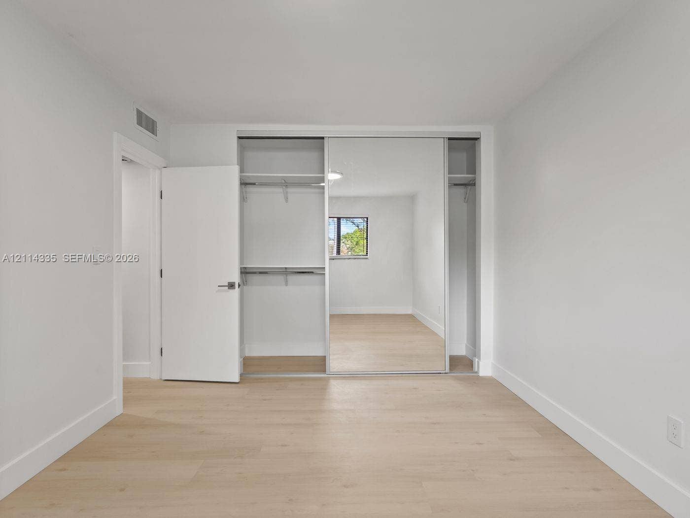 2930 Day Avenue, #N102, Miami, Miami, FL 33133 Neutral-toned interior featuring wood-finish flooring, sliding mirror-door closet with built-in shelving, and a solid-core swing door