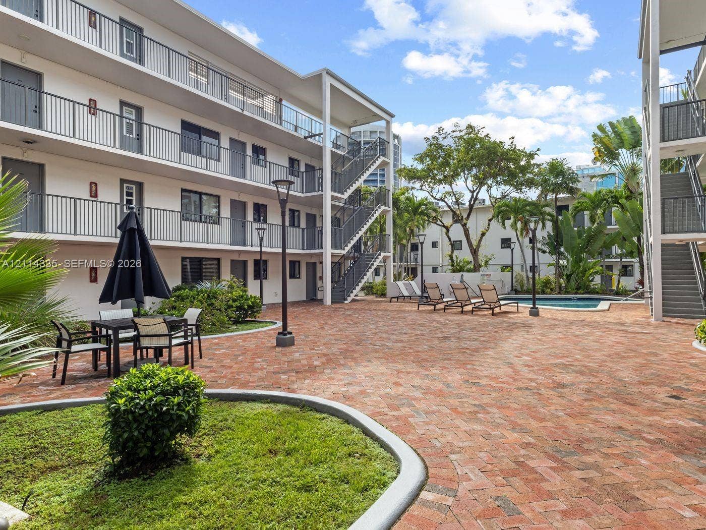 2930 Day Avenue, #N102, Miami, Miami, FL 33133 Courtyard featuring brick paver hardscaping, swimming pool, mature palm trees, multi-level metal staircases, and exterior catwalks
