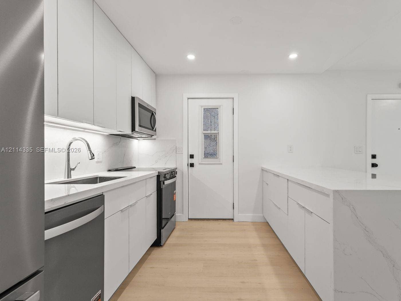 2930 Day Avenue, #N102, Miami, Miami, FL 33133 Kitchen featuring flat-panel cabinetry, light-toned stone-finish countertops, stainless steel appliances, and wood-finish flooring