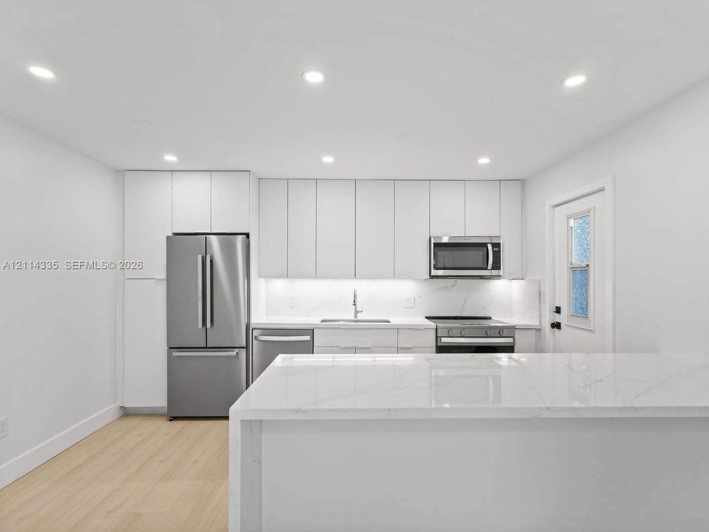 2930 Day Avenue, #N102, Miami, Miami, FL 33133 Kitchen featuring flat-panel cabinetry, a waterfall-edge stone island, stainless steel appliances, recessed ceiling lighting, and wood-finish flooring