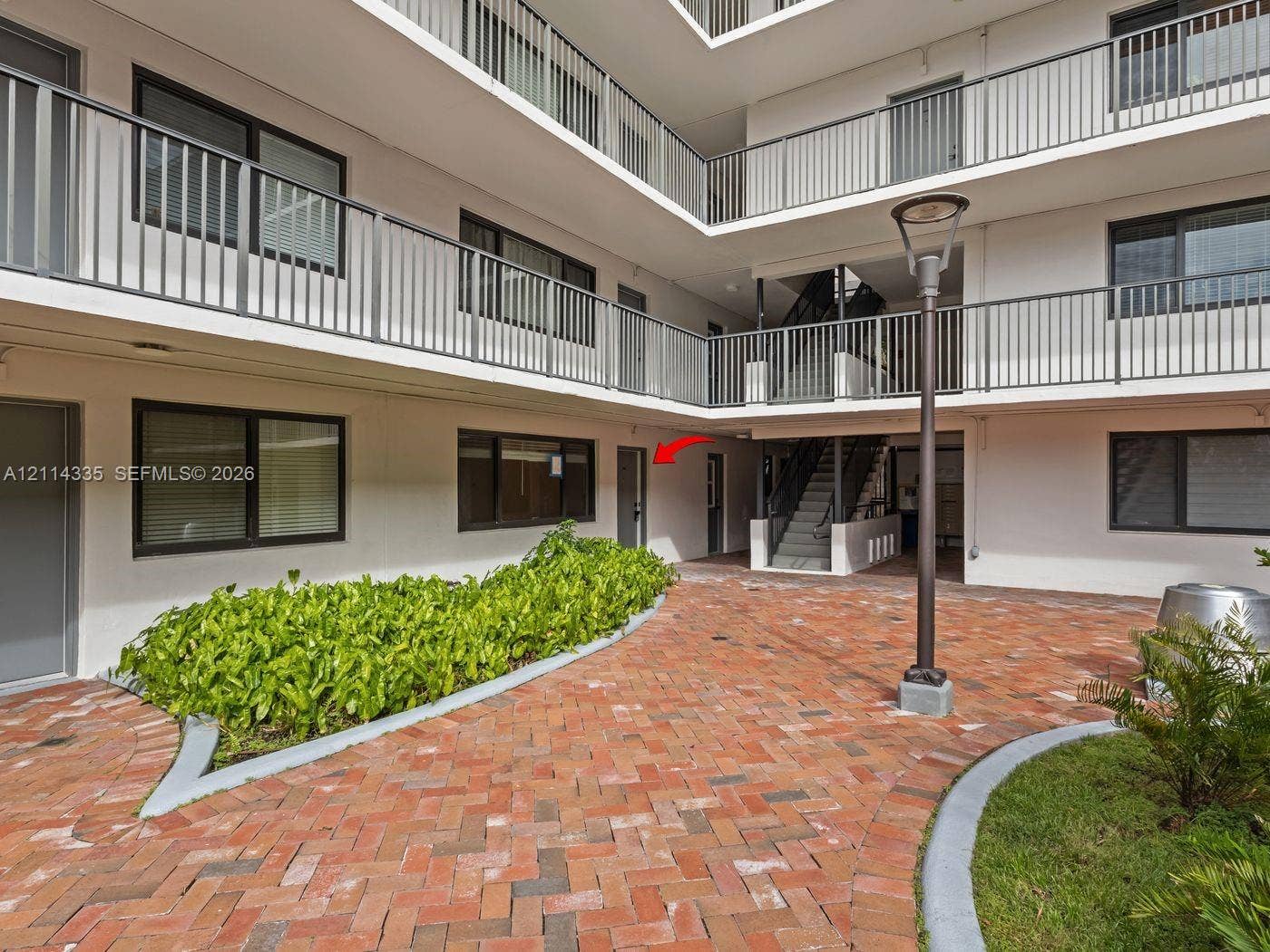2930 Day Avenue, #N102, Miami, Miami, FL 33133 Courtyard featuring herringbone-patterned brick pavers, integrated landscape beds, tiered structural metal balconies, and a built-in metal light fixture