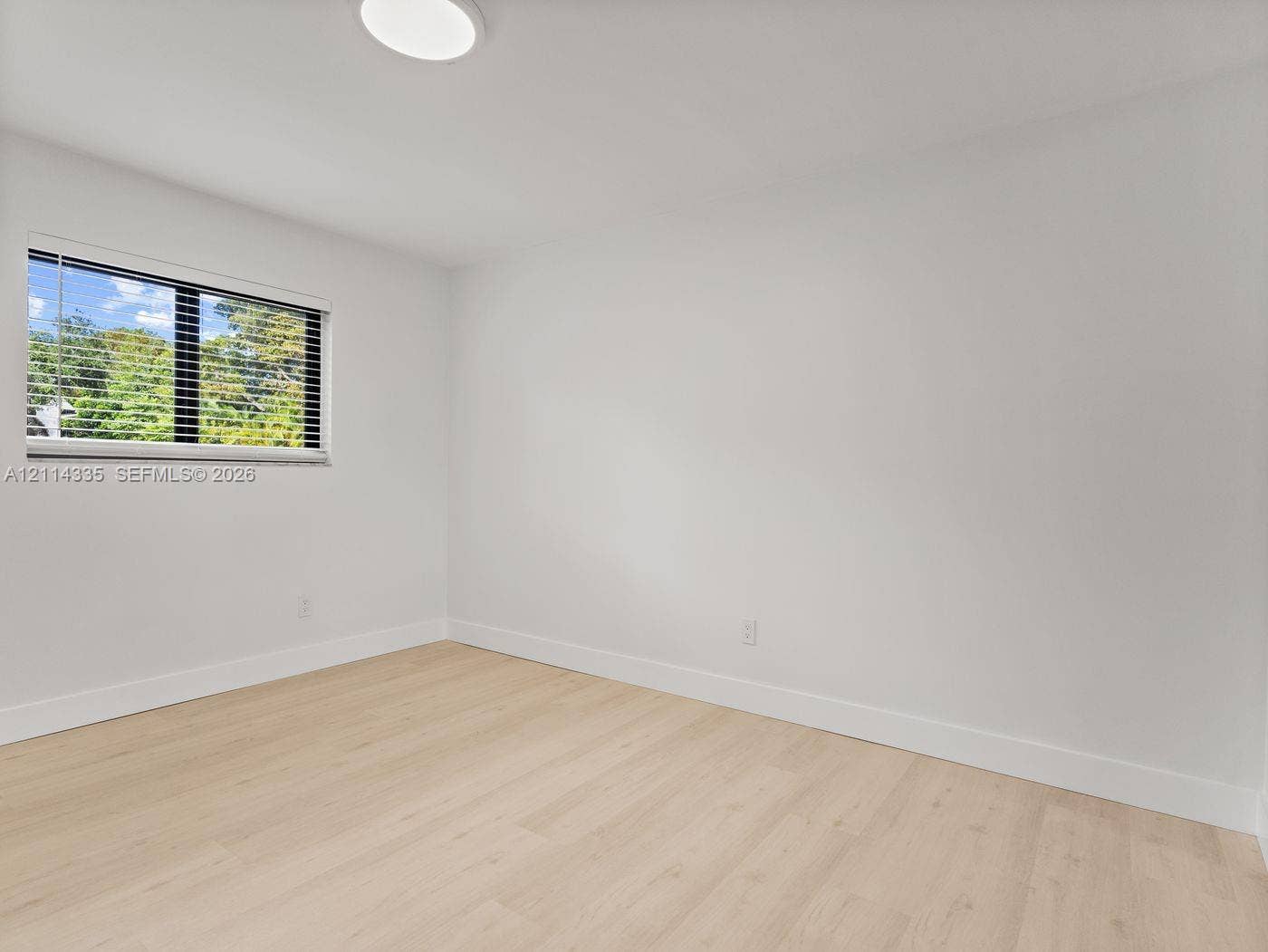 2930 Day Avenue, #N102, Miami, Miami, FL 33133 Light-filled room featuring wood-finish flooring, a flush-mount circular ceiling light, and a single-pane horizontal window with integrated blinds