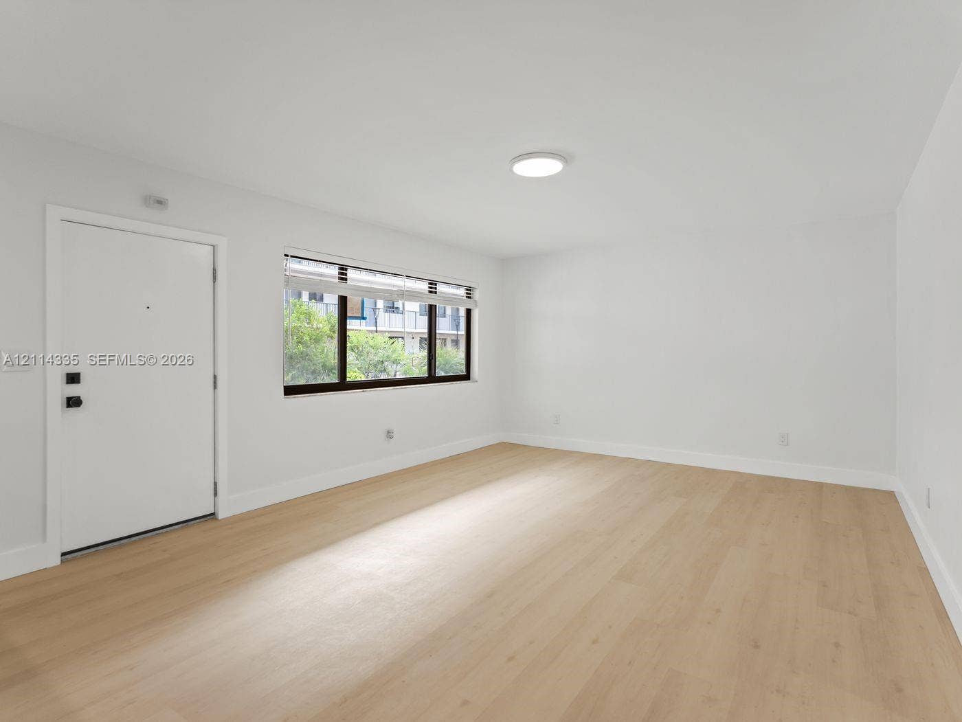 2930 Day Avenue, #N102, Miami, Miami, FL 33133 Neutral-toned space featuring wood-finish flooring, a flush-mount ceiling light, a white entry door with matte black hardware, and a window with a dark frame