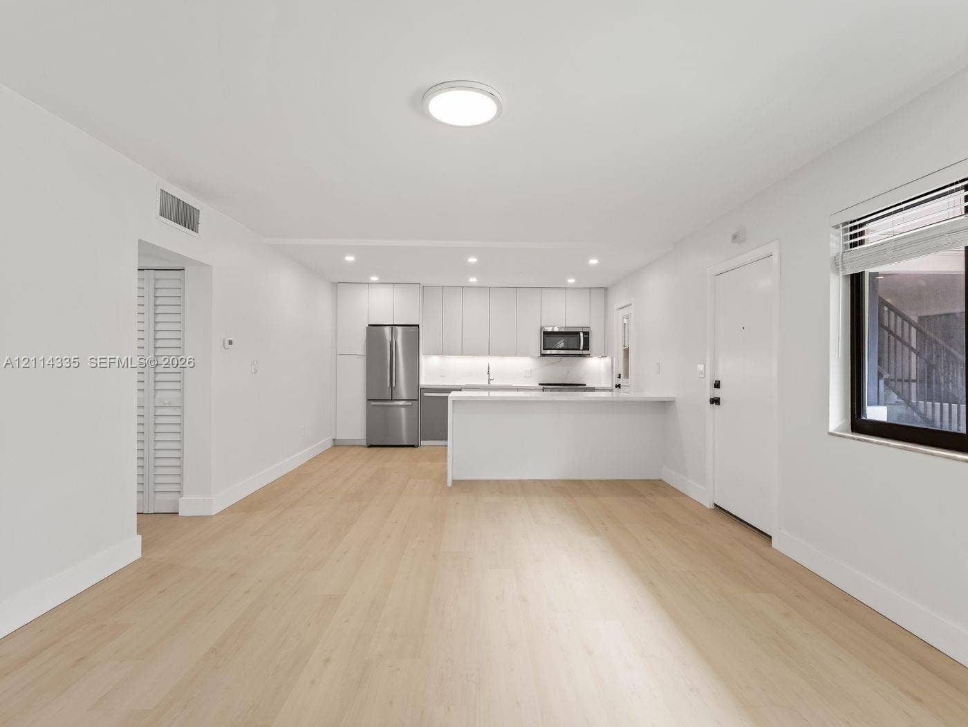 2930 Day Avenue, #N102, Miami, Miami, FL 33133 Open-concept area featuring light wood-finish flooring, white flat-panel cabinetry, a stainless steel refrigerator, a built-in microwave, and a white breakfast bar
