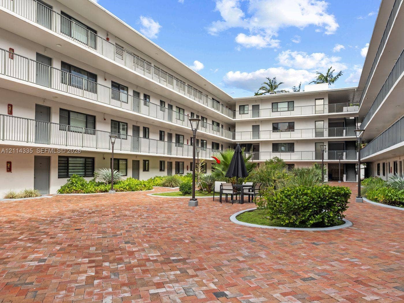 2930 Day Avenue, #N102, Miami, Miami, FL 33133 Courtyard featuring herringbone-pattern brick paving, multi-story building exterior with metal railings, and integrated landscaping with manicured shrubs