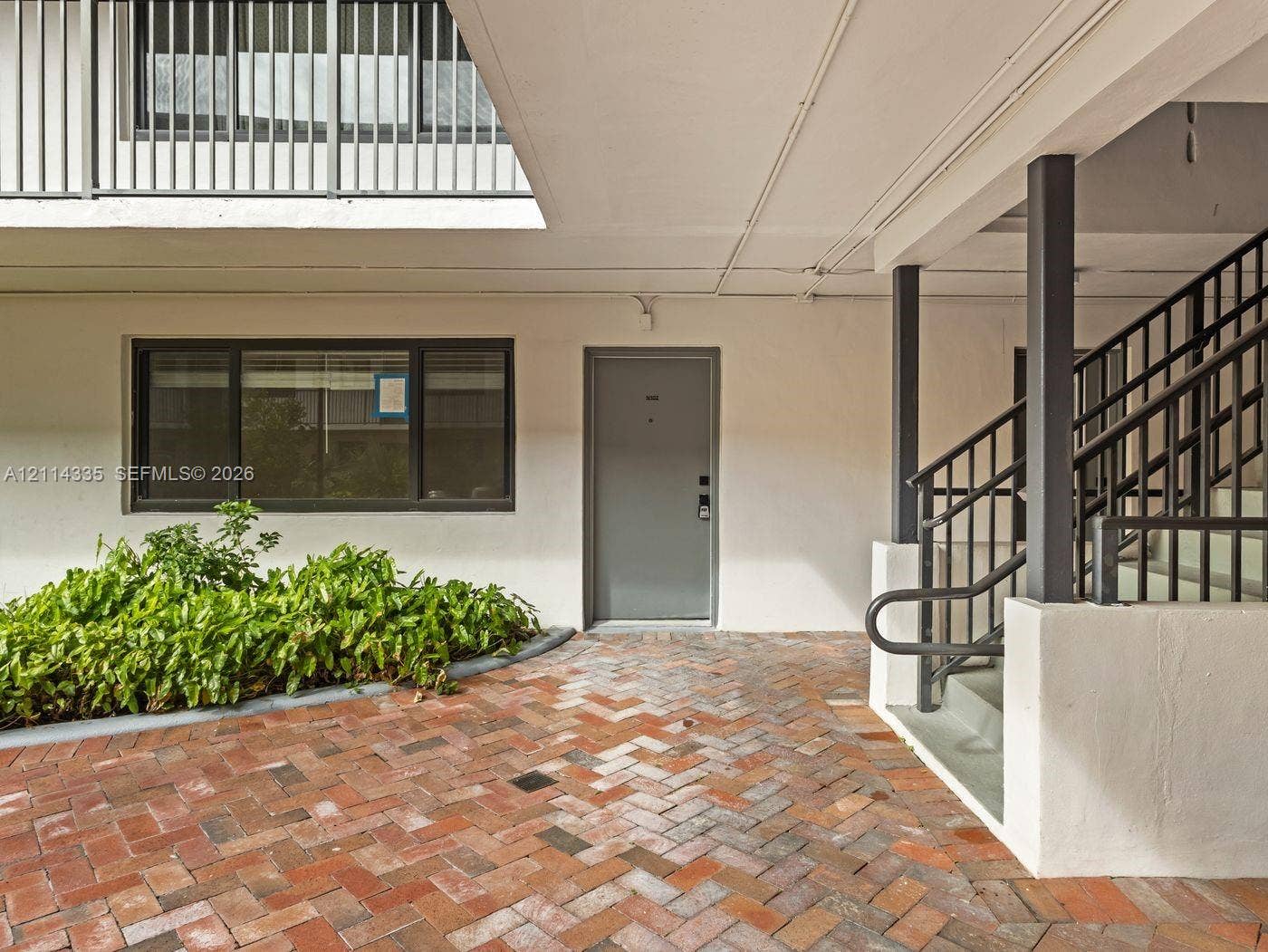 2930 Day Avenue, #N102, Miami, Miami, FL 33133 Herringbone brick courtyard featuring a metal staircase, smooth stucco exterior walls, dark-framed windows, and integrated landscaping