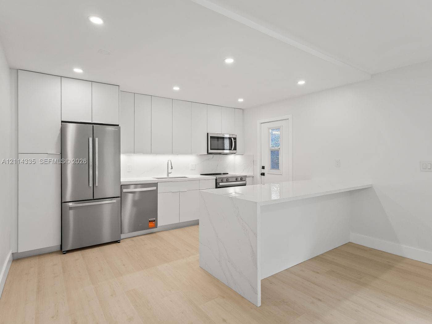 2930 Day Avenue, #N102, Miami, Miami, FL 33133 Modern kitchen featuring floor-to-ceiling cabinetry, a waterfall-edge island, integrated stainless steel appliances, recessed lighting, and wood-finish flooring