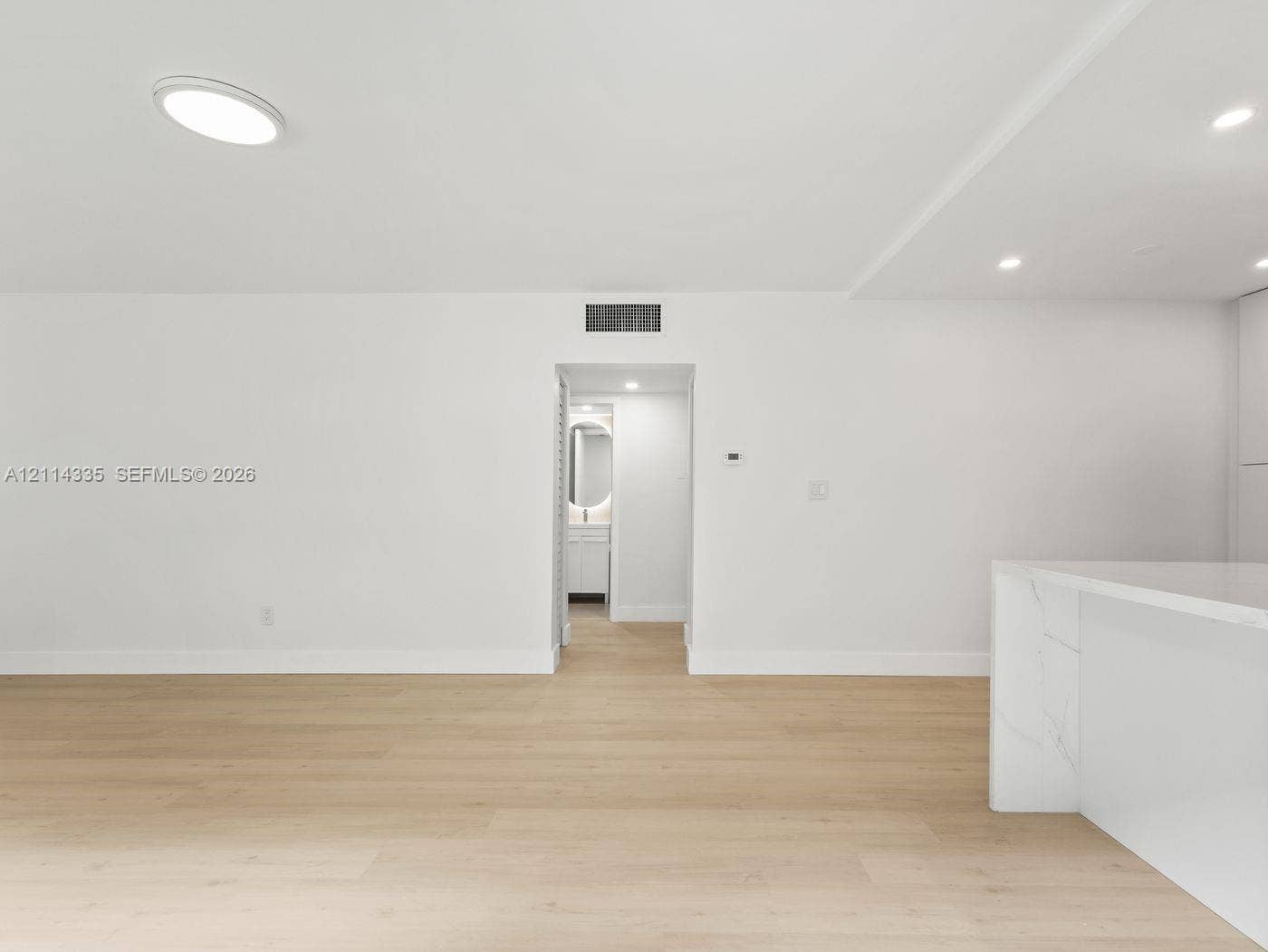 2930 Day Avenue, #N102, Miami, Miami, FL 33133 Neutral-toned interior space featuring light wood-finish flooring, recessed ceiling lighting, and a stone-surface waterfall edge island with integrated cabinetry