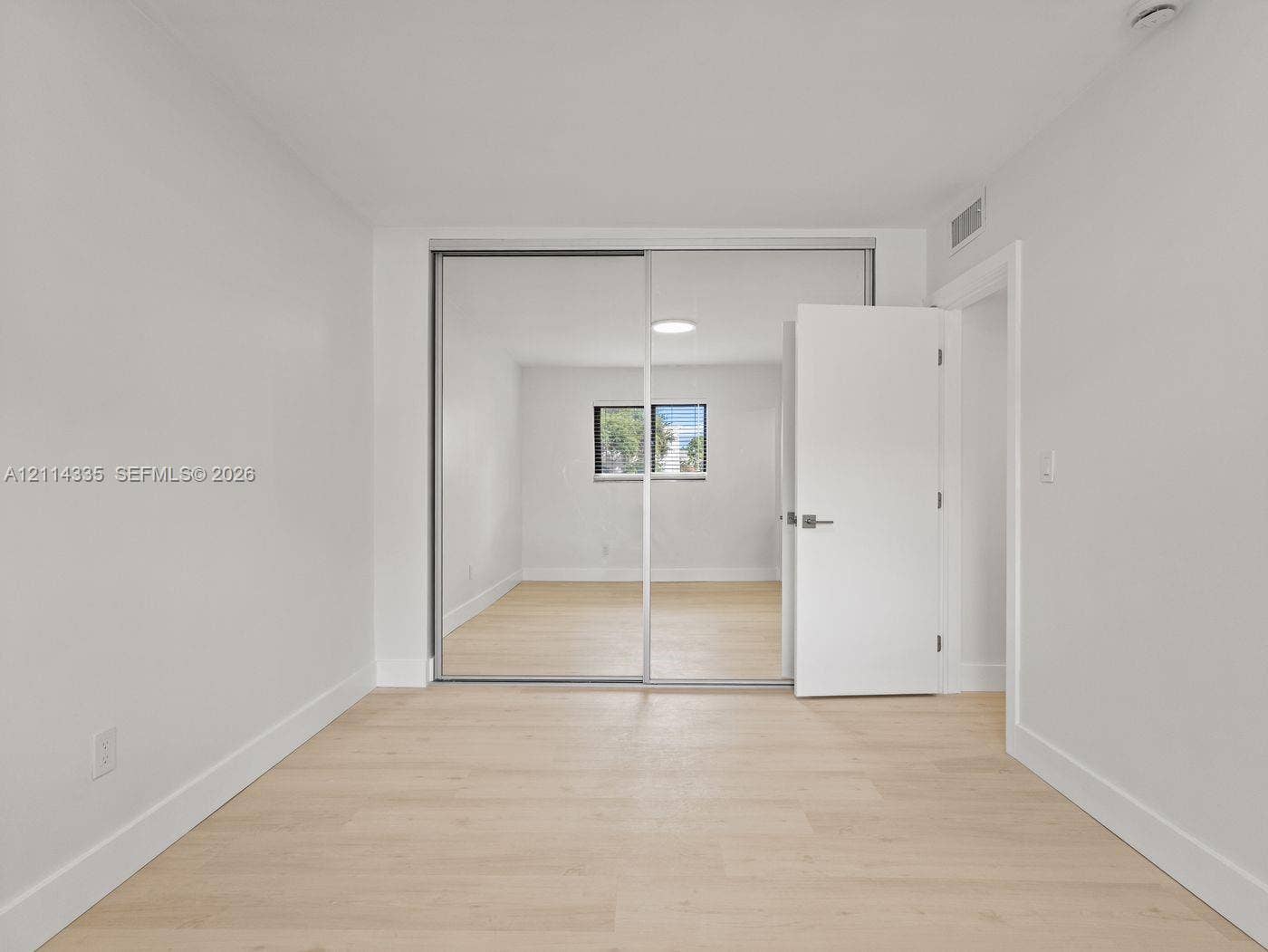 2930 Day Avenue, #N102, Miami, Miami, FL 33133 Interior room featuring light wood-finish flooring, white walls, and floor-to-ceiling mirrored sliding closet doors
