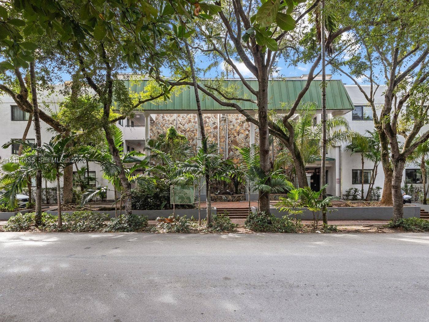 2930 Day Avenue, #N102, Miami, Miami, FL 33133 Multi-story exterior featuring a prominent green metal roof, natural stone facade, structural columns, and mature landscaping