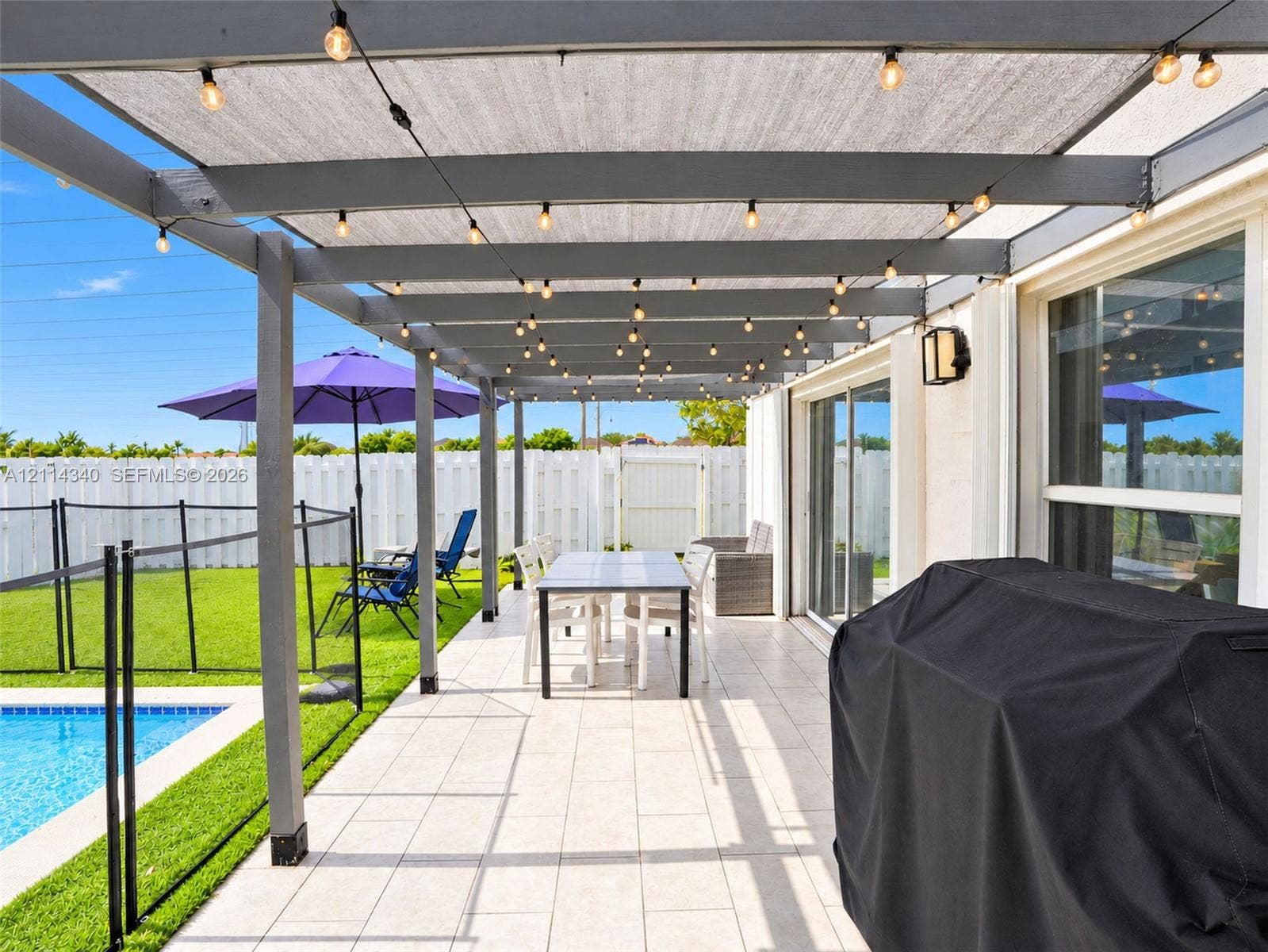 3586 SW 50th Street, Hollywood, FL 33312 Outdoor patio featuring a gray-painted wood pergola with a sunshade canopy, tile flooring, and integrated string lighting