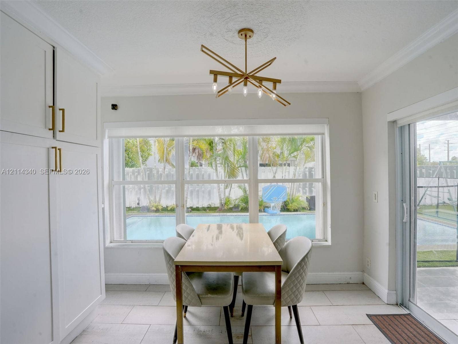3586 SW 50th Street, Hollywood, FL 33312 Dining area featuring built-in floor-to-ceiling cabinetry with metallic hardware, large multi-pane windows, gold-tone modern chandelier, and oversized ceramic tile flooring