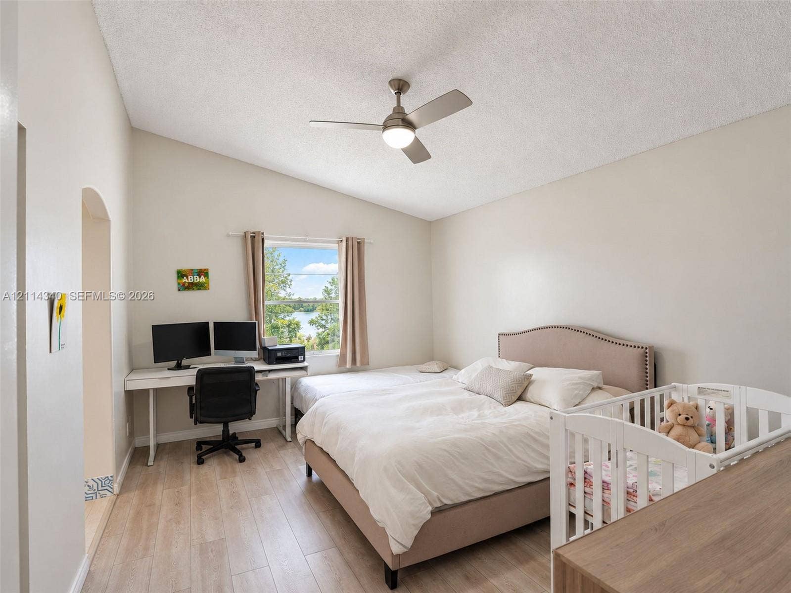 3586 SW 50th Street, Hollywood, FL 33312 Vaulted ceiling featuring a central brushed-metal ceiling fan with integrated light, wood-finish flooring, and natural light from a window with exterior water surroundings