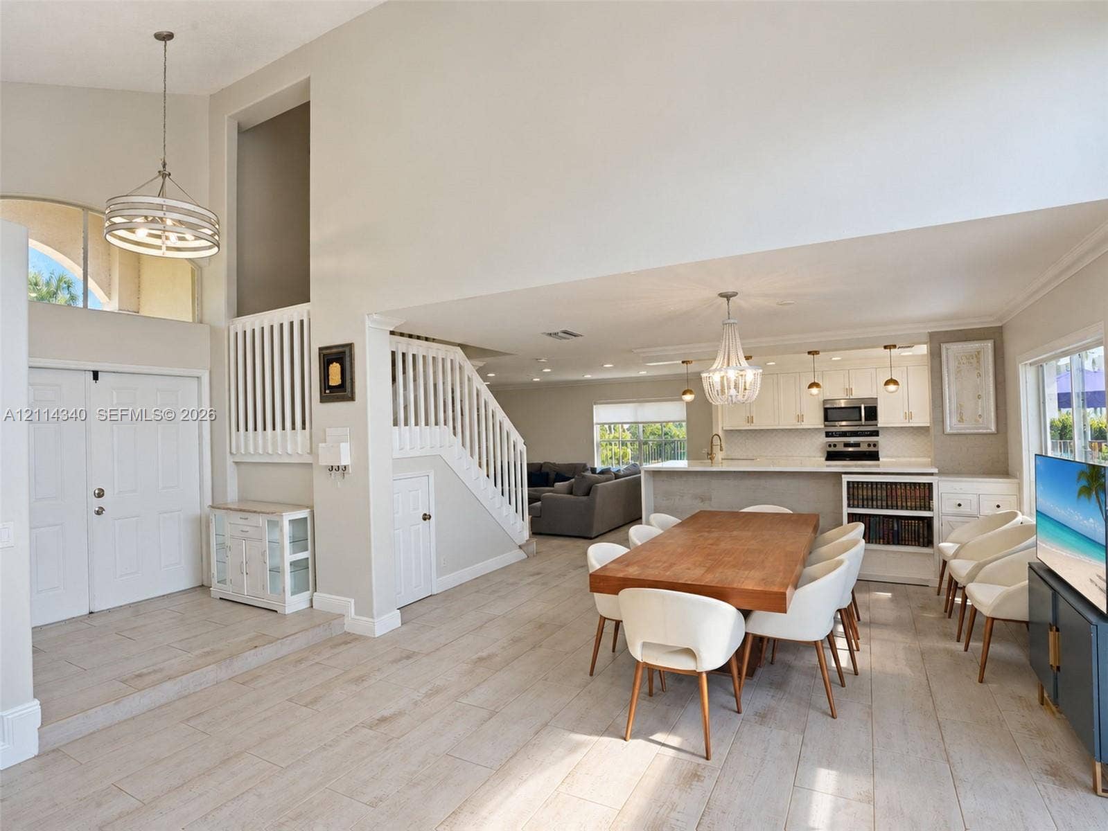 3586 SW 50th Street, Hollywood, FL 33312 Open-concept interior featuring vaulted ceilings, wood-finish flooring, a tiered staircase with white balusters, and a kitchen equipped with white cabinetry and a built-in oven