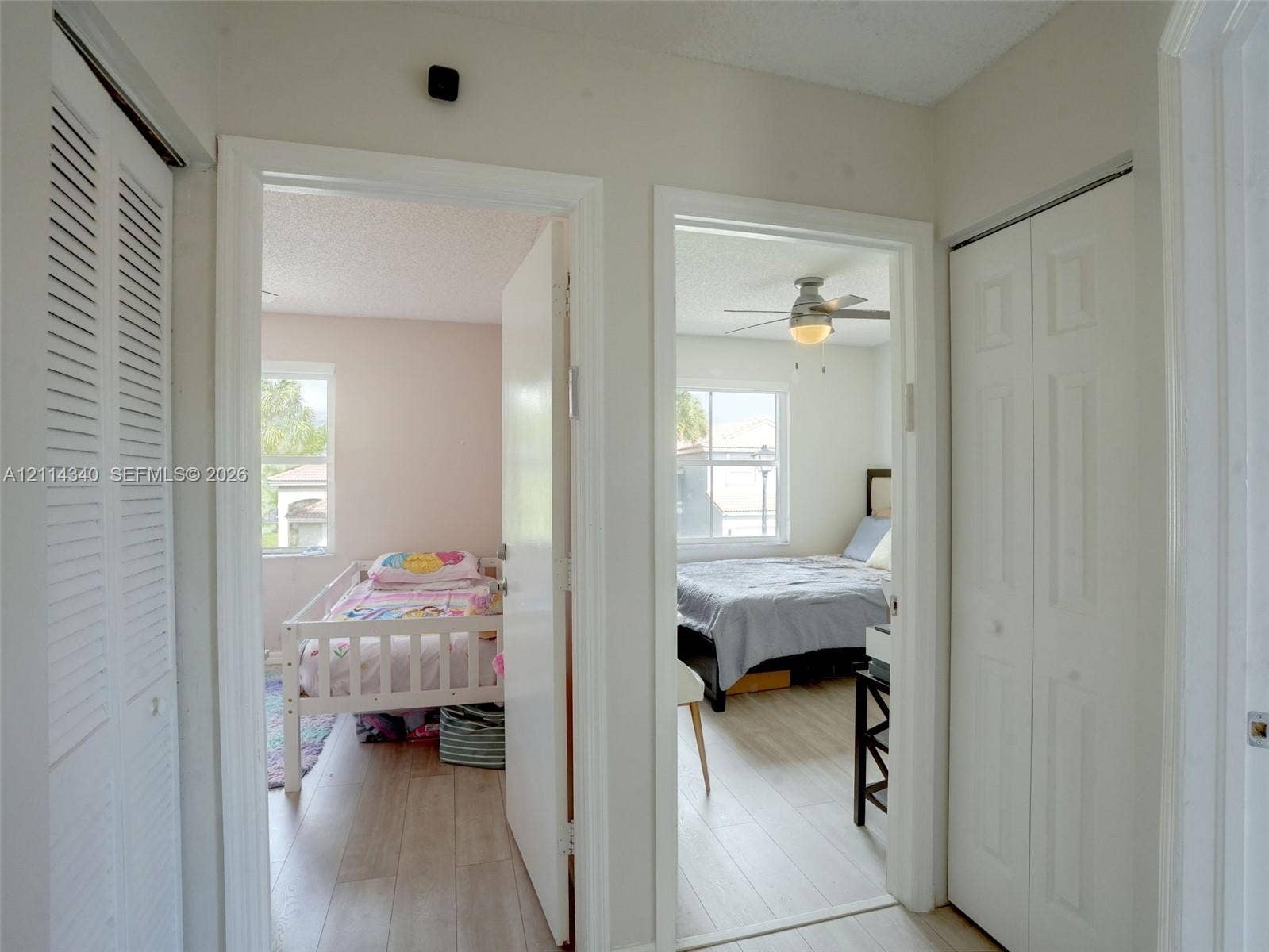3586 SW 50th Street, Hollywood, FL 33312 Hallway featuring two sets of white louvered-style bi-fold closet doors, wood-finish flooring, and two interior doorways with light-colored solid-core doors