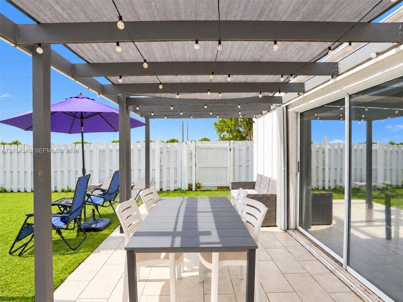 3586 SW 50th Street, Hollywood, FL 33312 Covered patio featuring a grey wooden pergola, tile flooring, and integrated string lighting, complemented by a white privacy fence