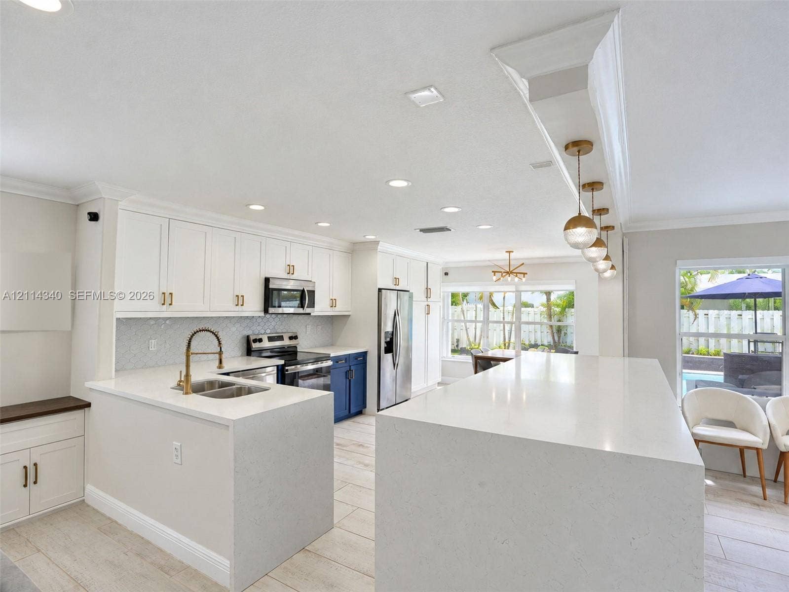3586 SW 50th Street, Hollywood, FL 33312 Kitchen featuring an oversized waterfall quartz island, custom white cabinetry with gold-tone hardware, a geometric tile backsplash, stainless steel appliances, and recessed lighting