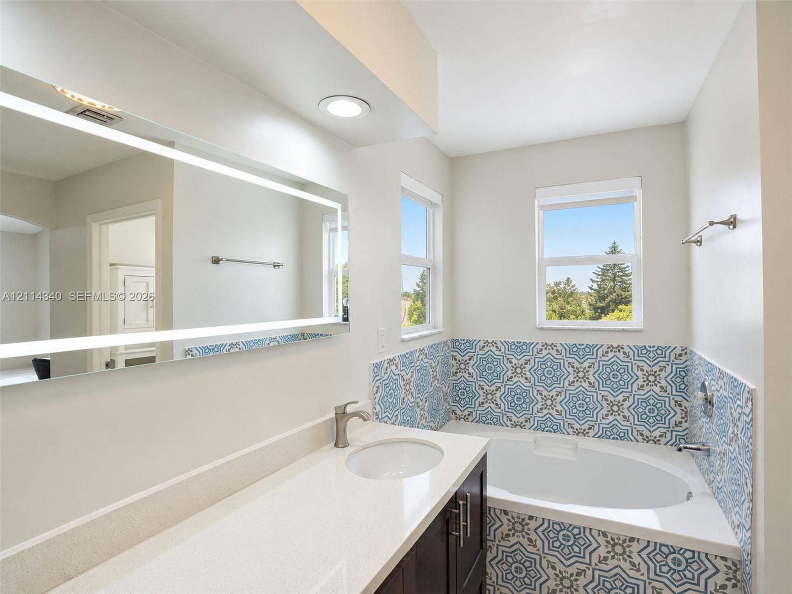 3586 SW 50th Street, Hollywood, FL 33312 Built-in vanity with white solid-surface countertop and undermount sink, integrated backlit mirror, recessed lighting, and jetted soaking tub featuring patterned ceramic tile surround