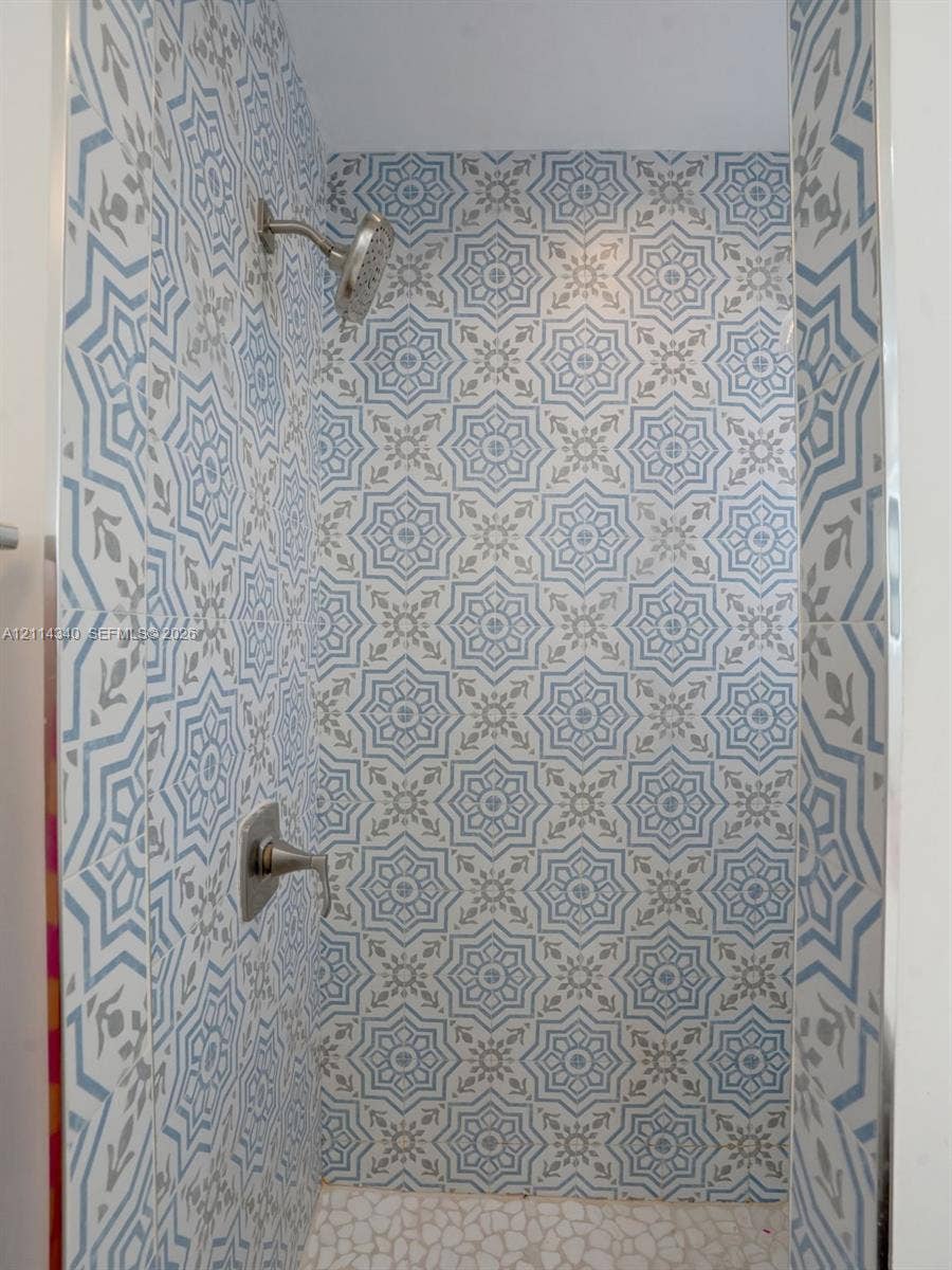 3586 SW 50th Street, Hollywood, FL 33312 Shower stall featuring patterned blue and white tile wall accents, a pebble-finish floor, and brushed-finish plumbing fixtures