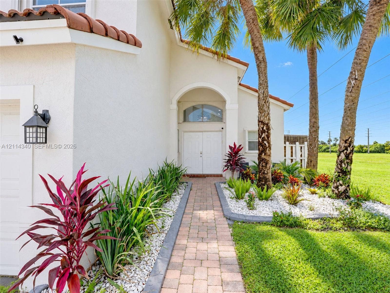 3586 SW 50th Street, Hollywood, FL 33312 Stucco exterior featuring a tiled roof, arched entryway with double doors, paver walkway, and professional landscaping with mature palm trees