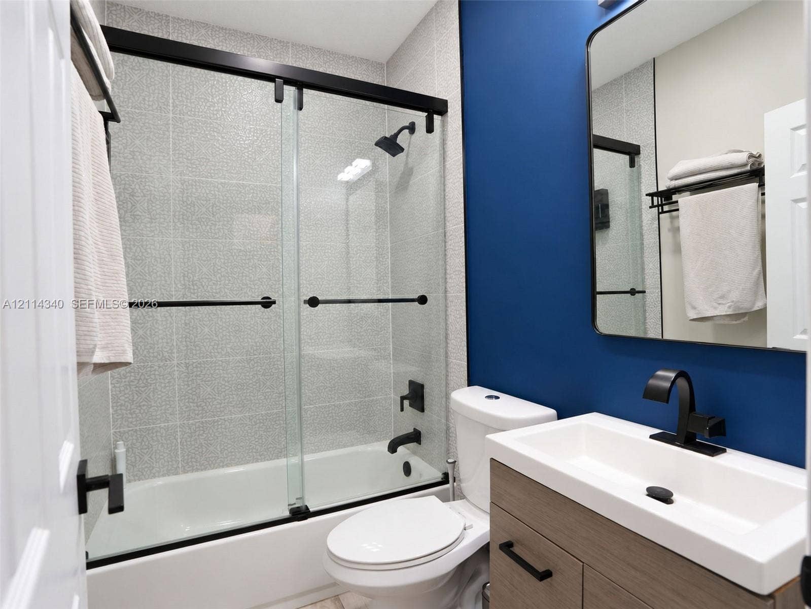 3586 SW 50th Street, Hollywood, FL 33312 Bathroom featuring a wood-finish vanity with a rectangular basin, matte black fixtures, a glass shower enclosure with sliding doors, and tiled shower surround