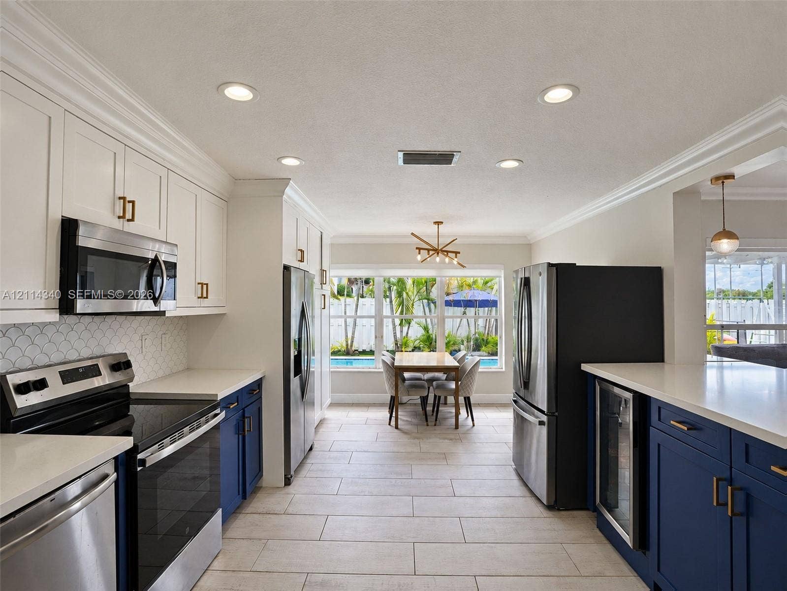 3586 SW 50th Street, Hollywood, FL 33312 Kitchen featuring white upper cabinetry, navy blue lower cabinetry, stainless steel appliances, quartz countertops, and scalloped tile backsplash