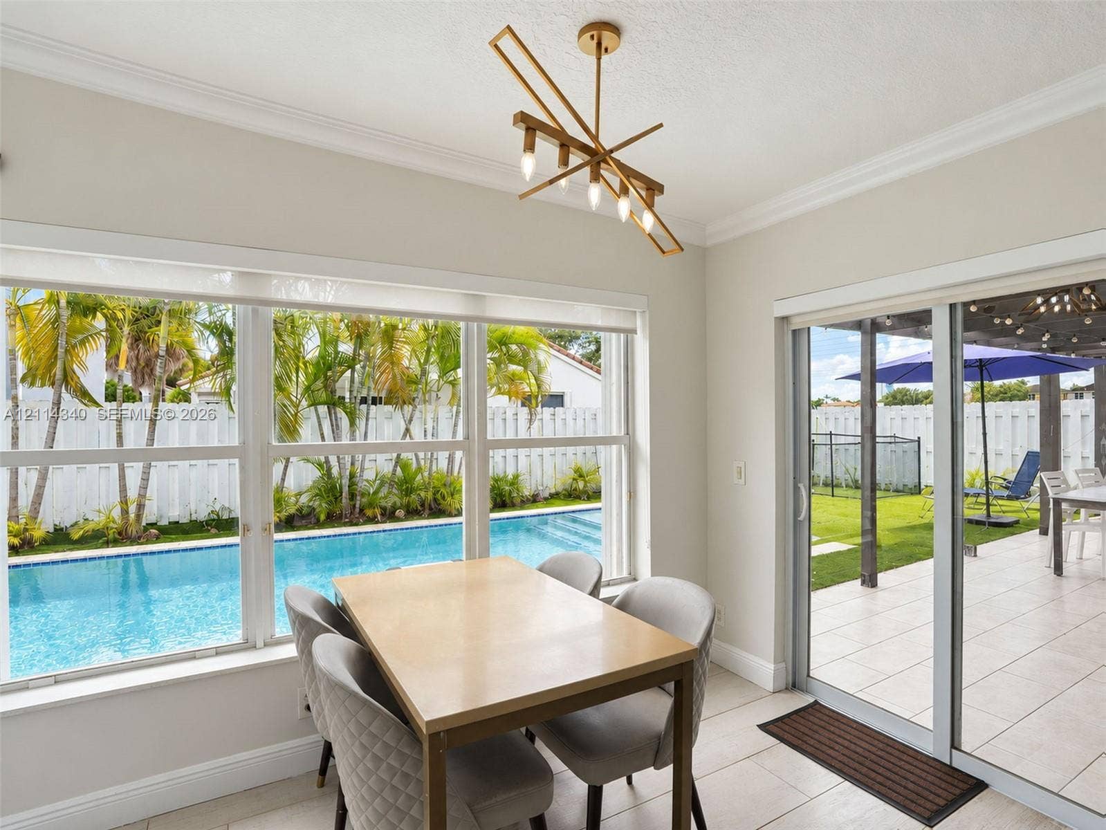 3586 SW 50th Street, Hollywood, FL 33312 Dining area featuring crown molding, an angular gold-tone multi-light chandelier, large windows, and a glass sliding door providing outdoor access to a tiled patio and swimming pool