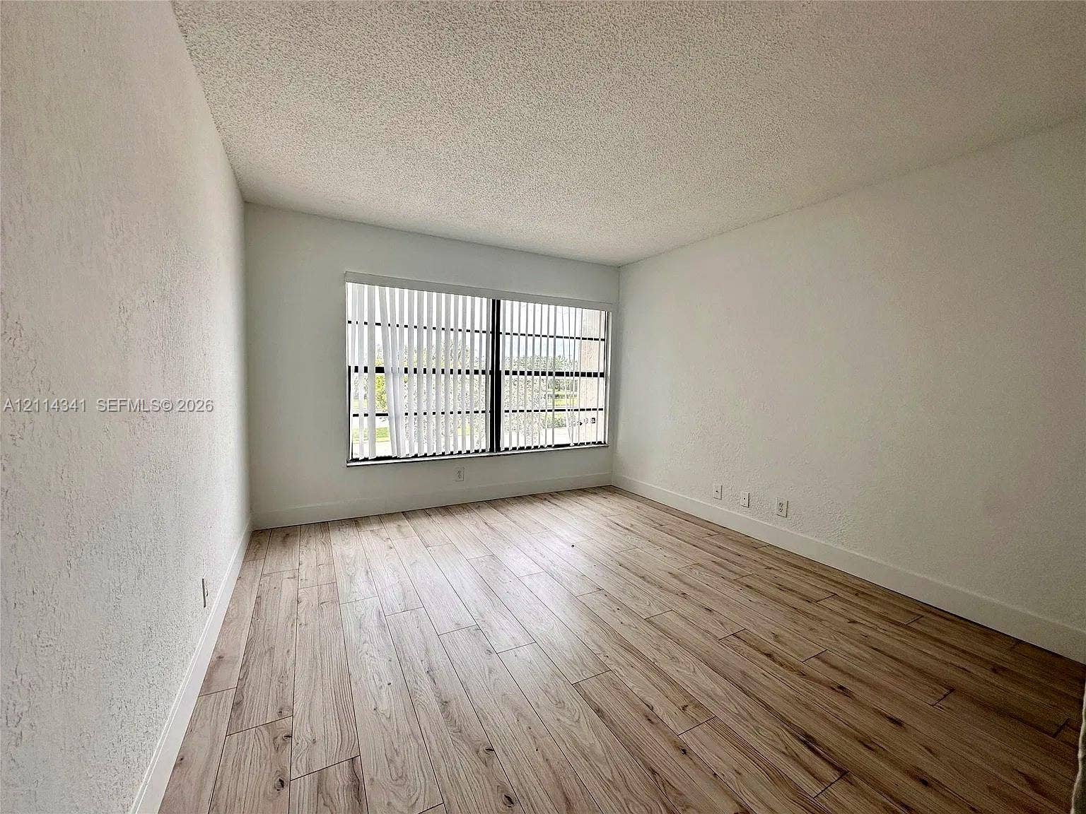 Interior space featuring wood-finish flooring, white walls, and a large window with vertical blinds