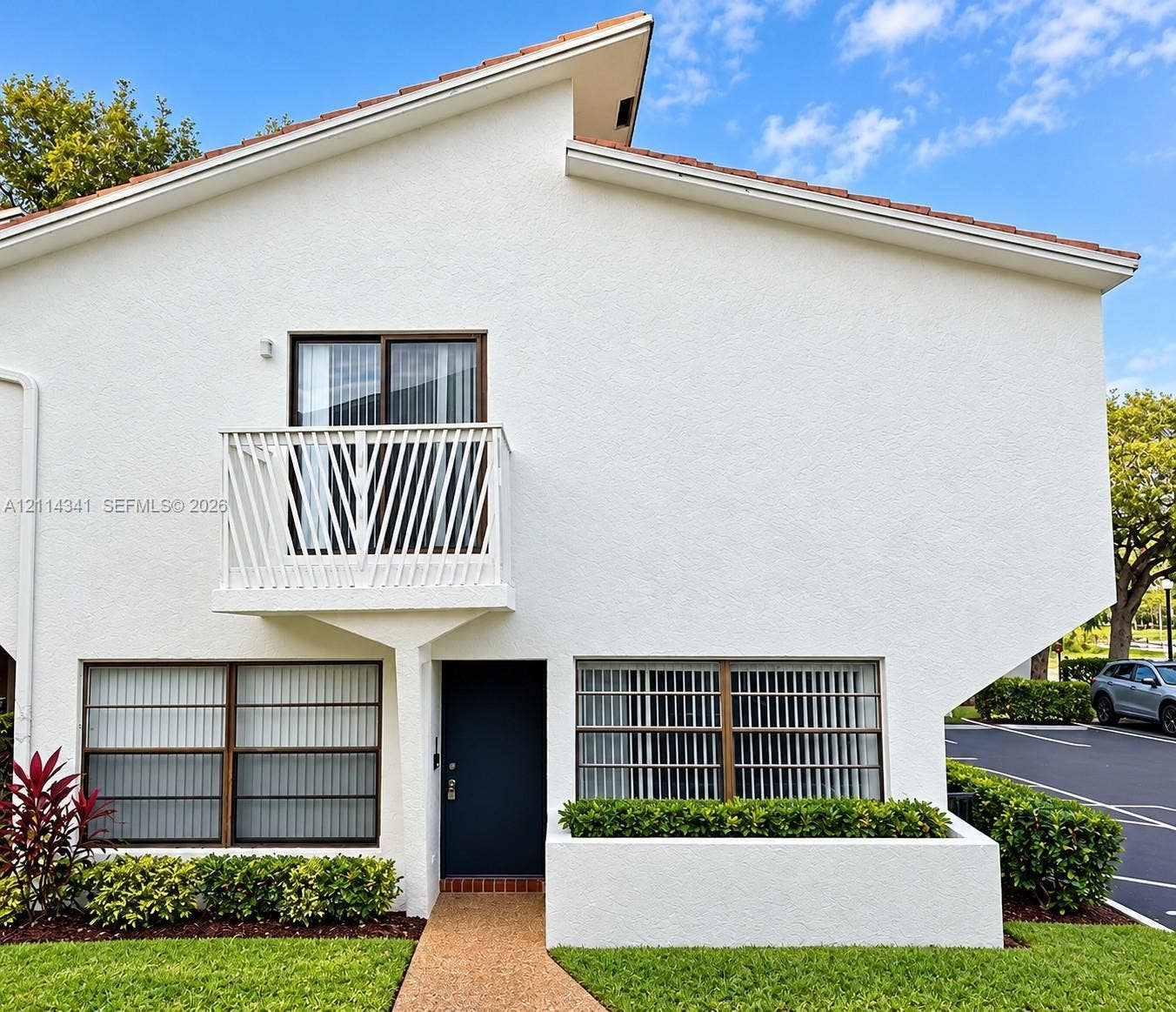 Stucco exterior featuring an asymmetric roofline, a second-story balcony with metal railing, and a built-in planter box