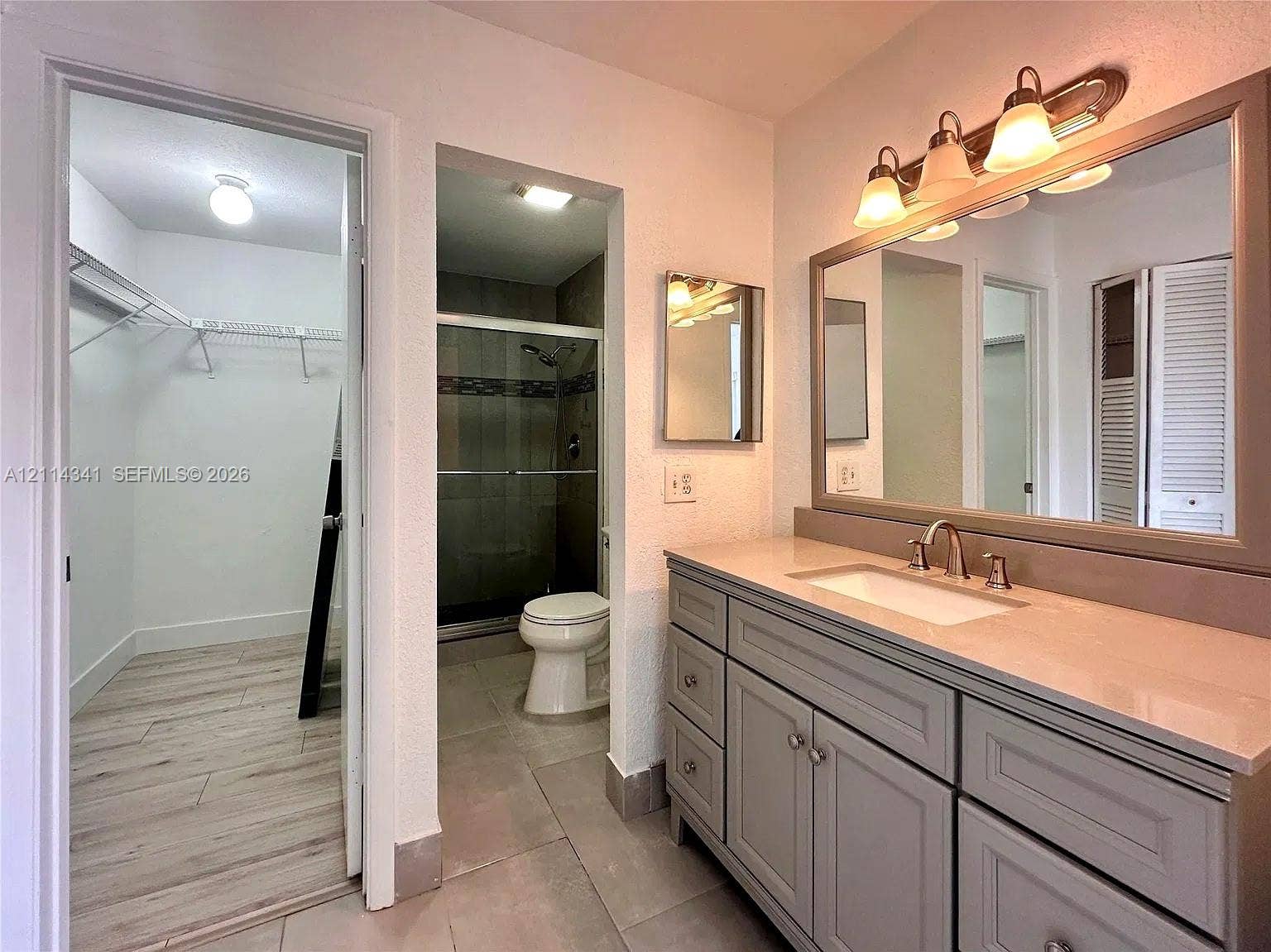 Bathroom featuring a vanity with shaker-style cabinetry, a solid-surface countertop with an integrated sink, a framed mirror, a multi-bulb light fixture, and a walk-in shower with tile surround